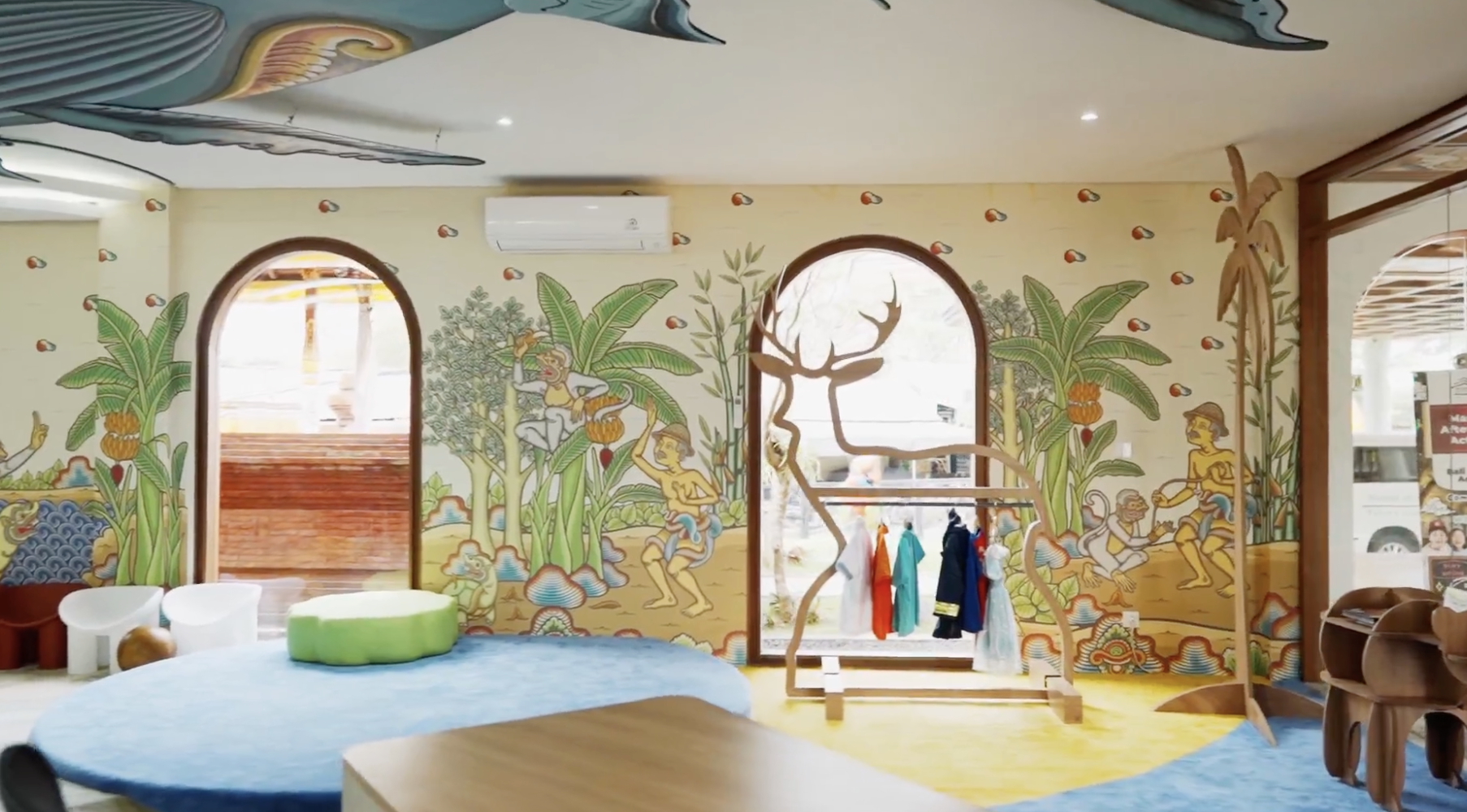 Colorful mural bathroom wall art featuring jungle scene with trees, animals, and playful children, including a monkey and a woman, with a window showing an outdoor view.