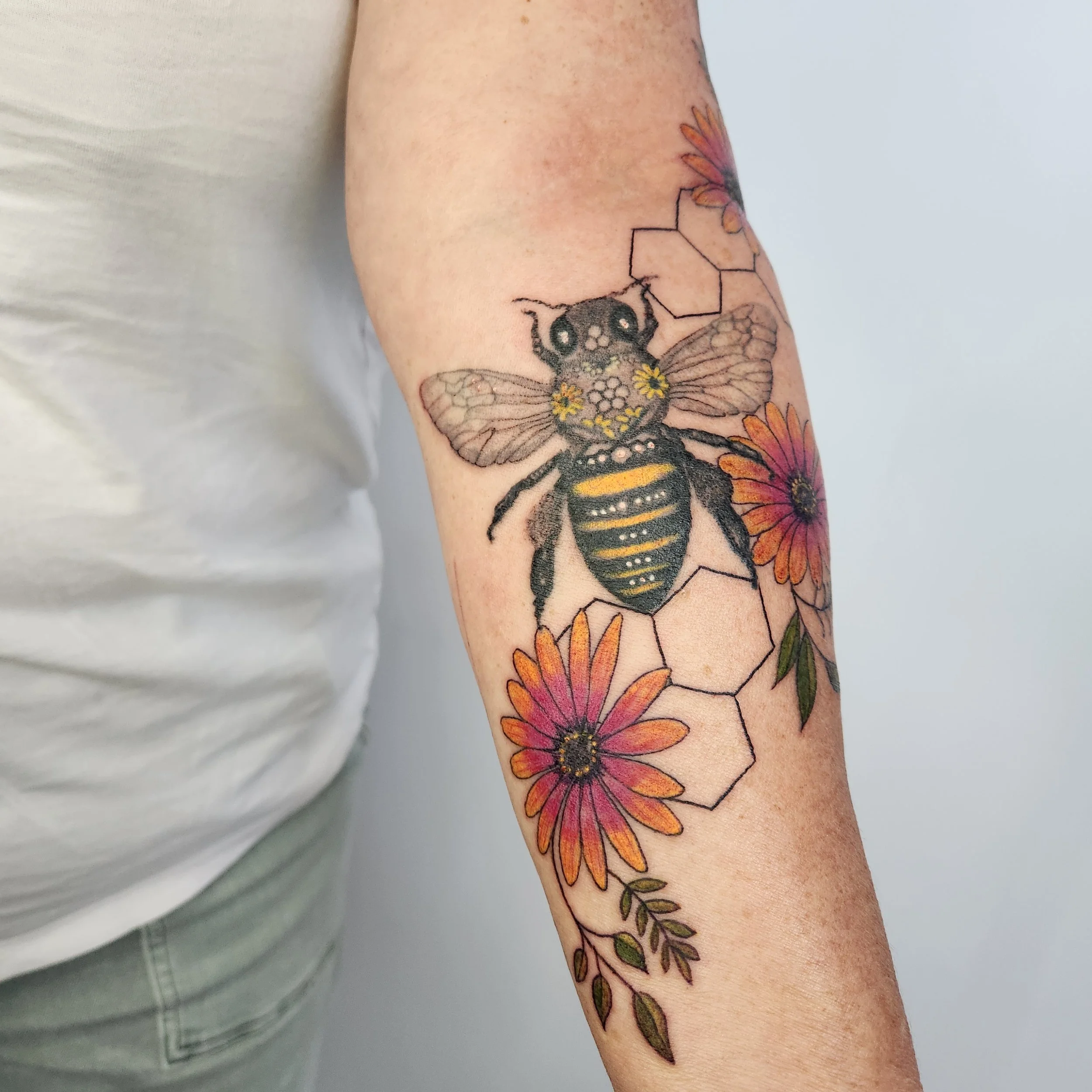 Tattoo of a bee with honeycomb and flowers on a person's arm.