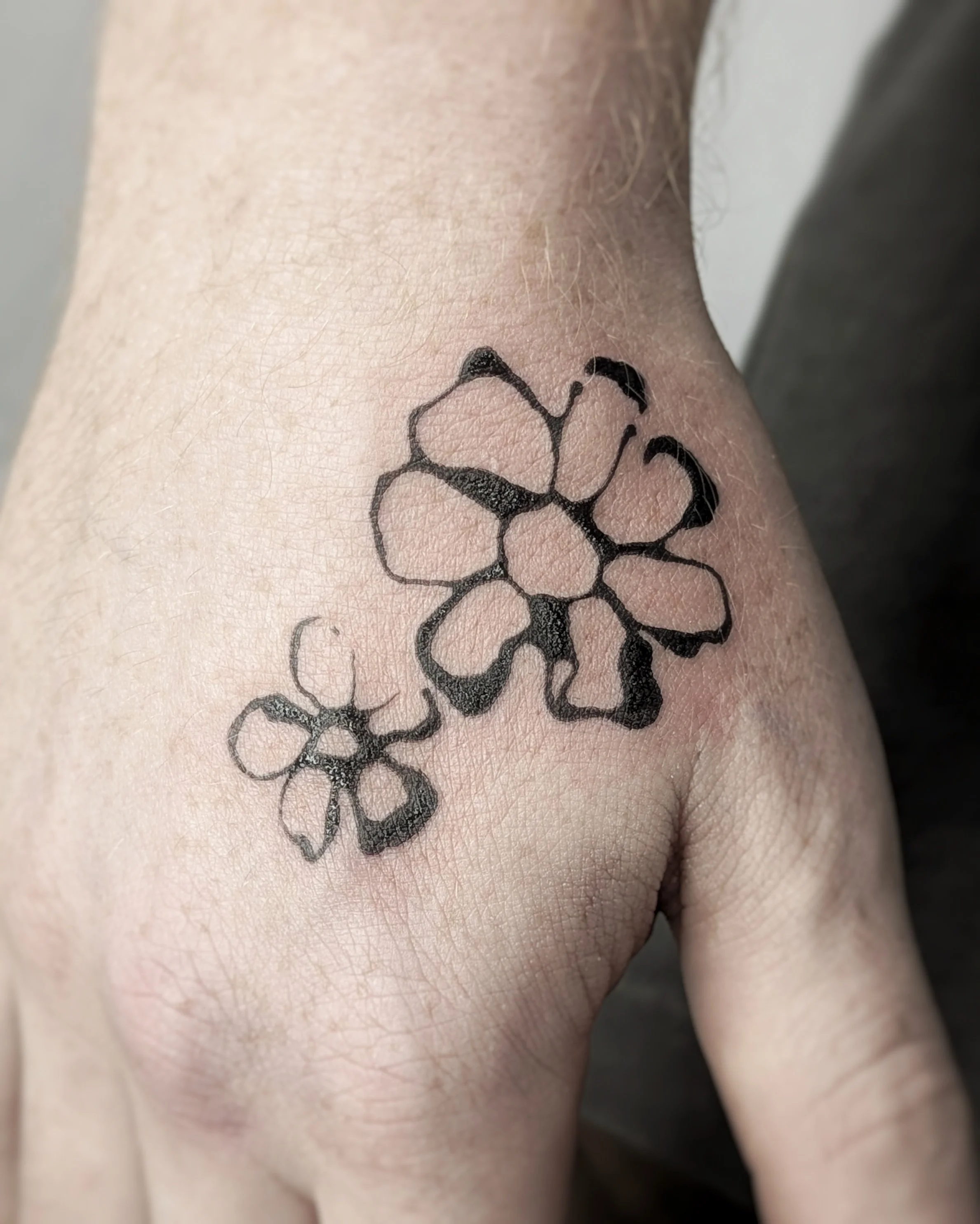 Black outline floral tattoo on person's shoulder with multiple flowers and leaves.