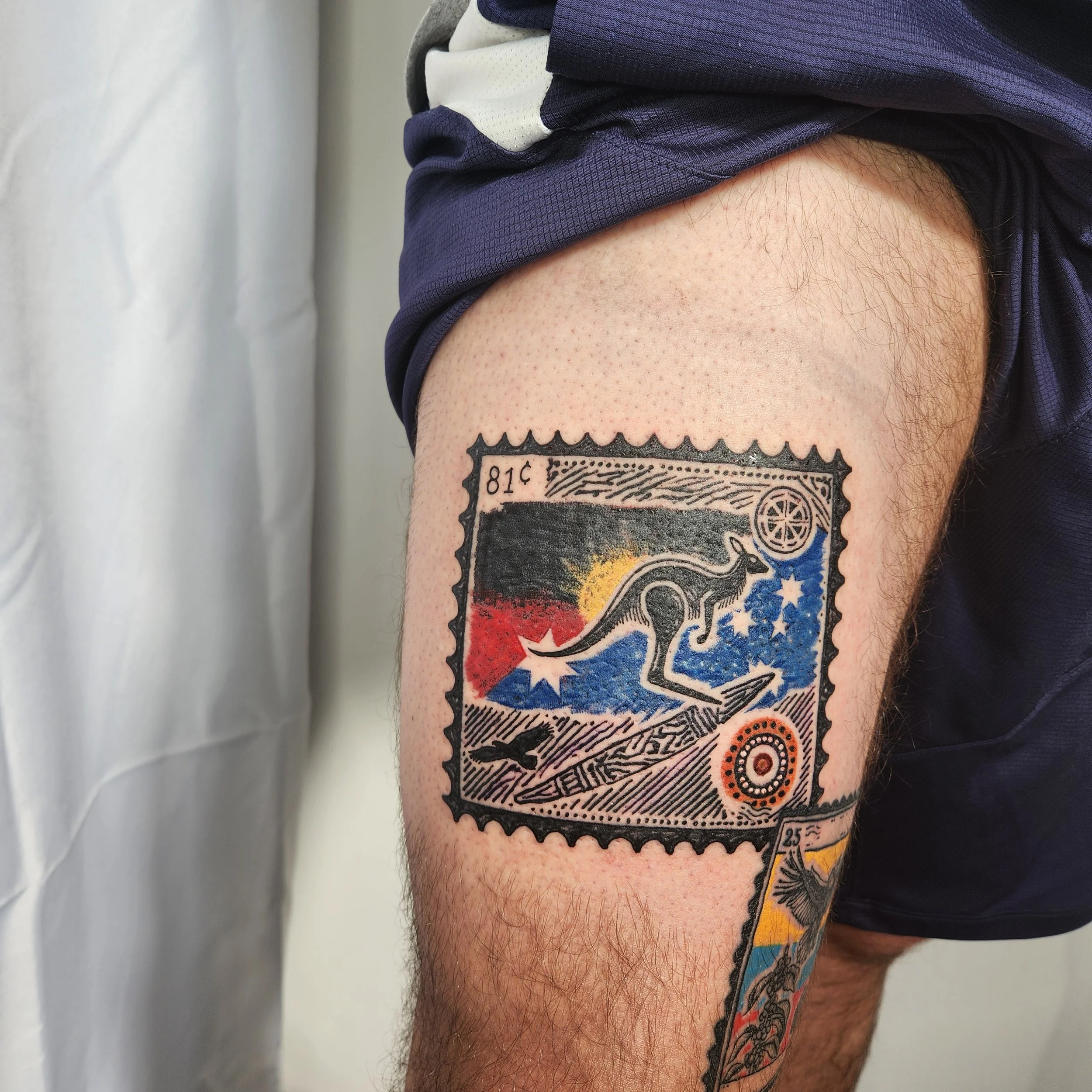 Colorful tattoo of a kangaroo on a postage stamp design on a person's upper thigh.