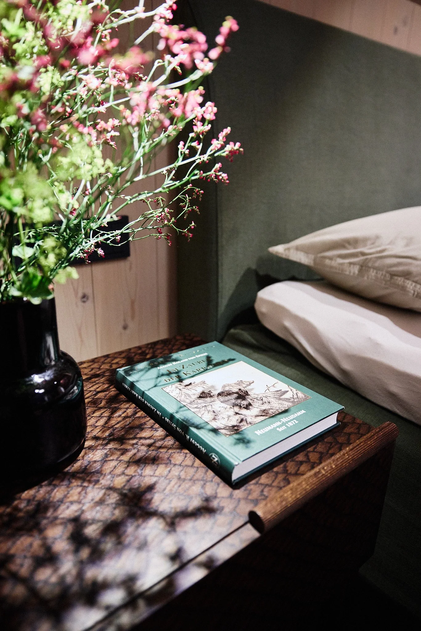 Detail im Schlafzimmer mit maßgefertigtem Nachtkästchen, grünem Polsterbett, Kunst und Blumen.