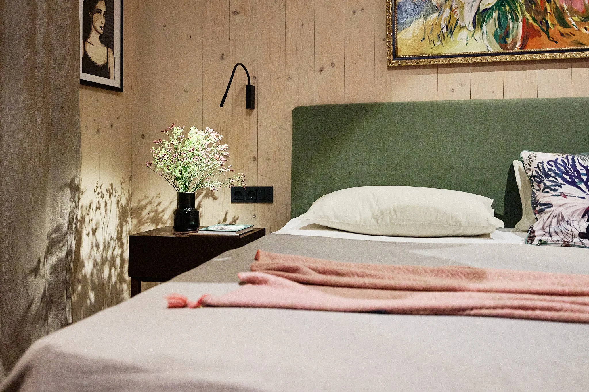 Schlafzimmer im Architektenhaus am See mit grünem Polsterkopfteil, Holzverkleidung, Kunst und maßgefertigtem Nachtkästchen.