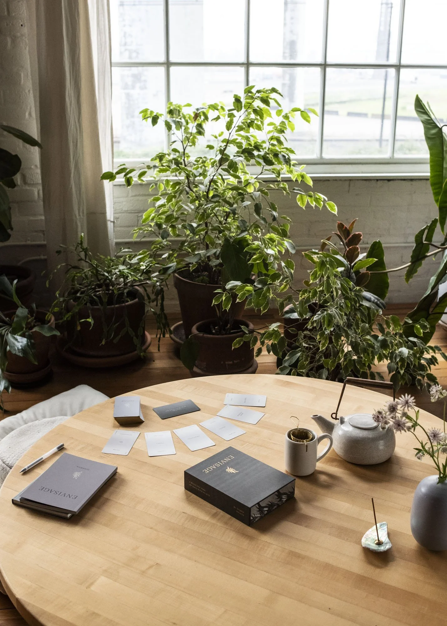 Envisage deck in use on table next to a pot of tea and flowers by light filled window surrounded by plants.