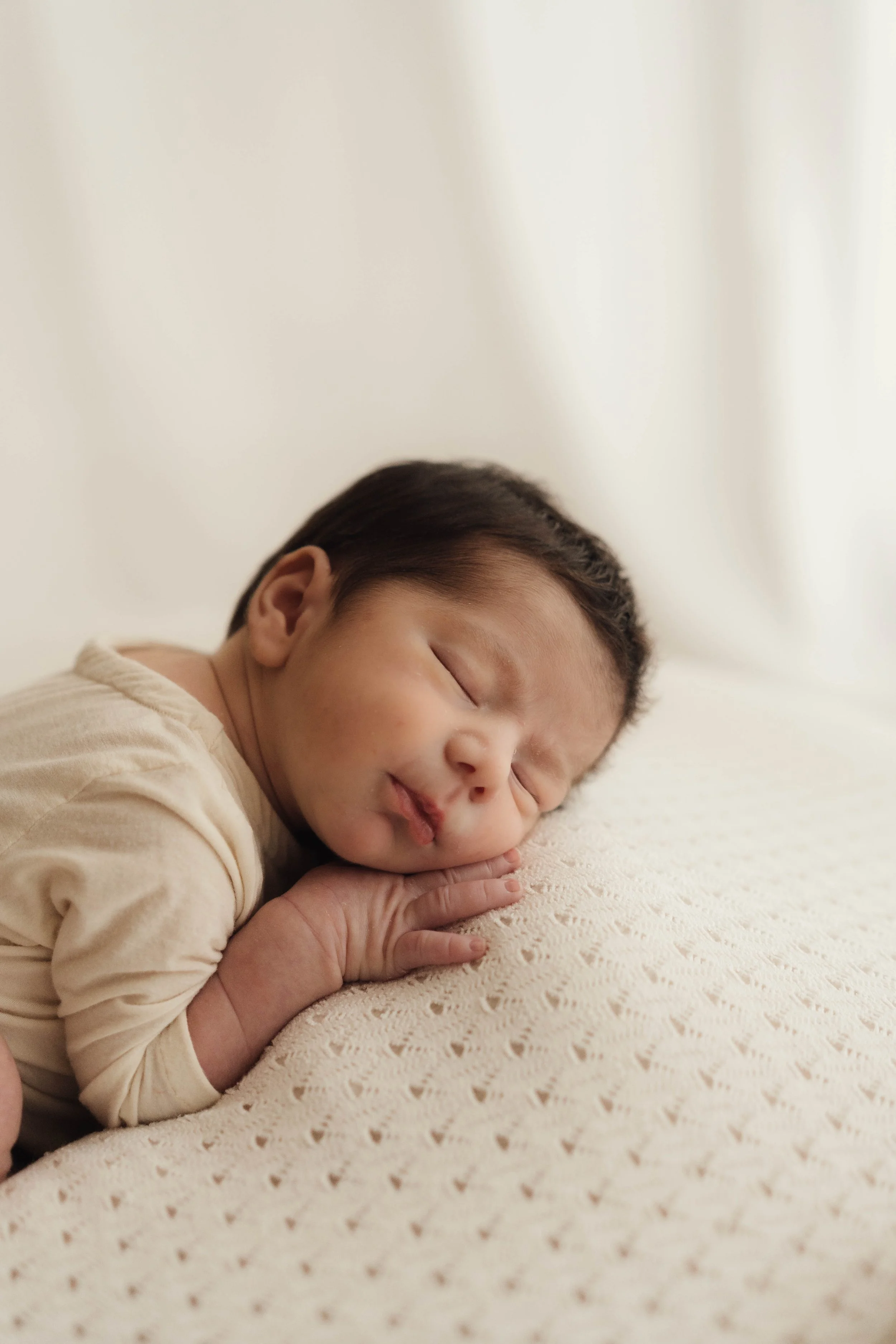 Un neonato che dorme avvolto in una coperta color crema.