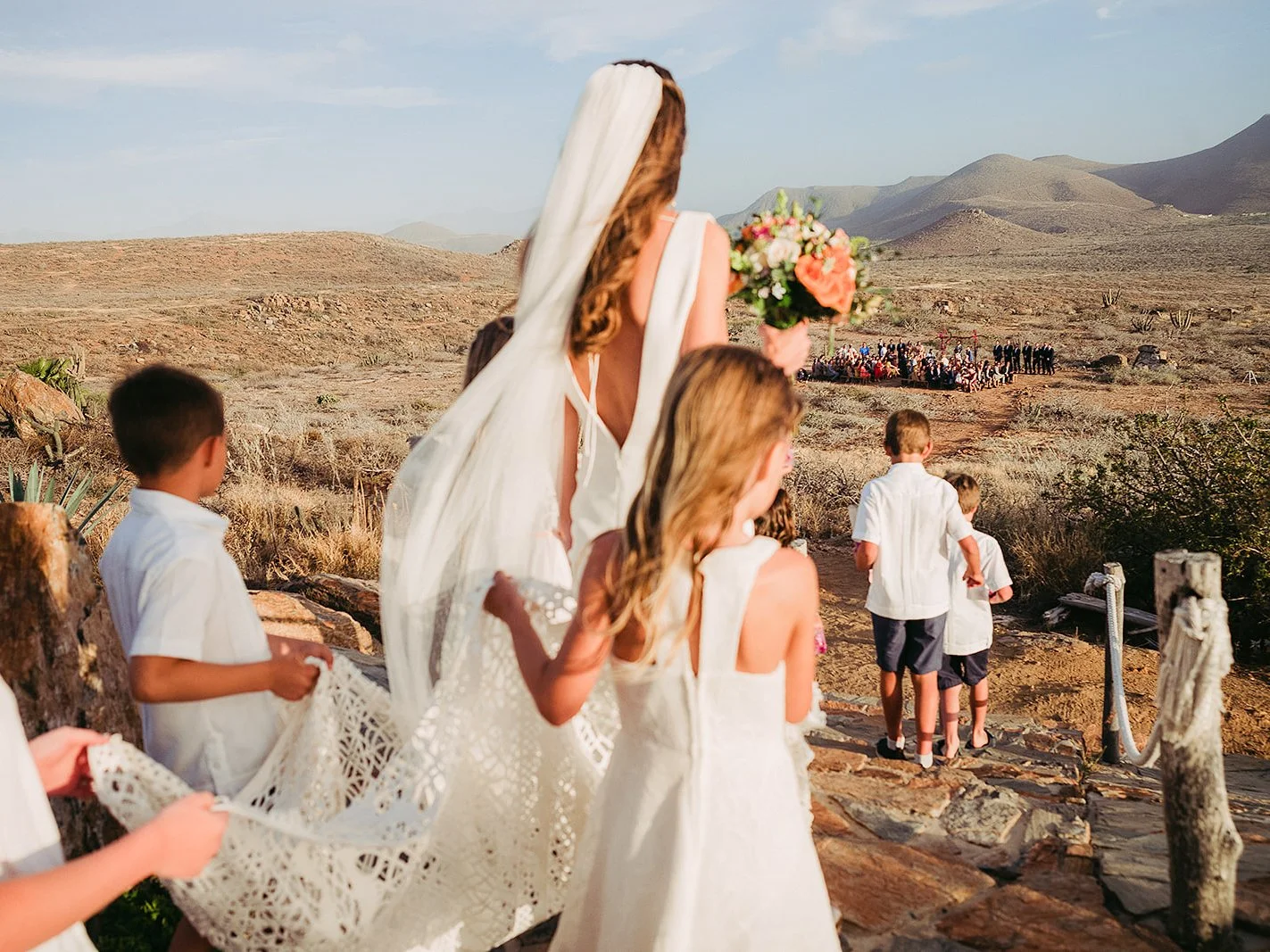 Children carry the bride's lace train down a desert path to a ceremony in Baja California, Mexico