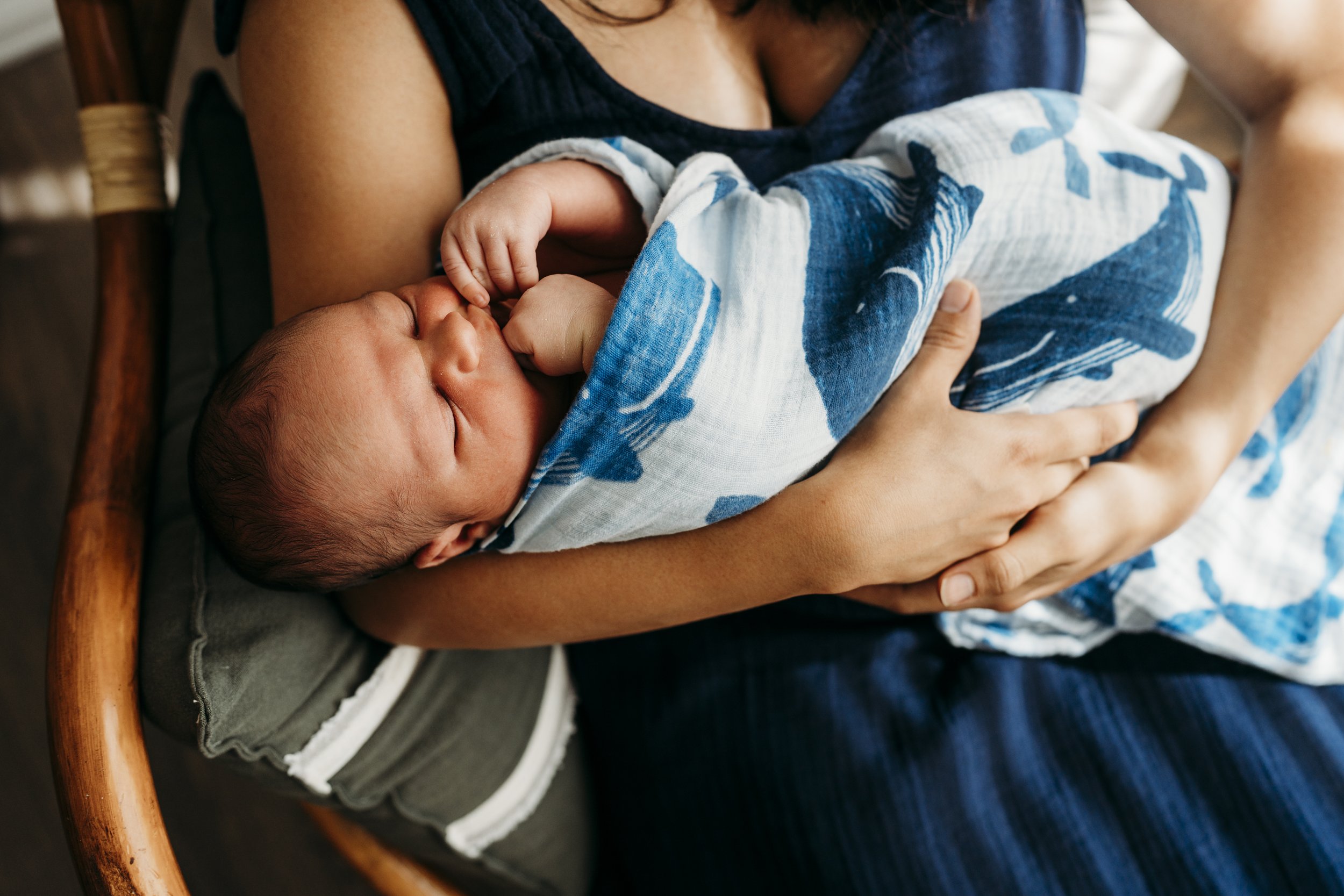 A person holding a sleeping baby wrapped in a blue and white blanket.