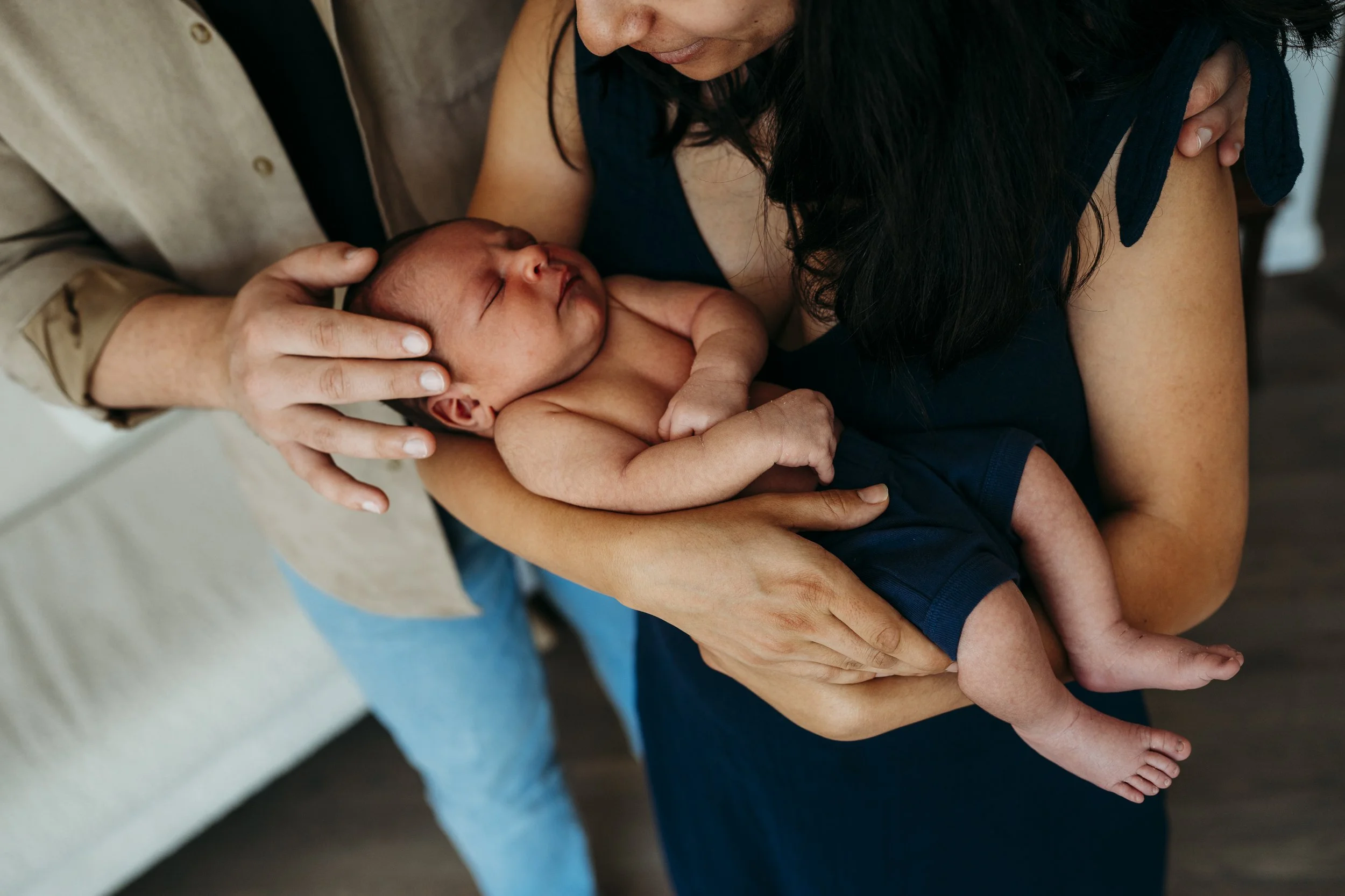 A woman holding a sleeping newborn baby in her arms while a man gently touches the baby's forehead.