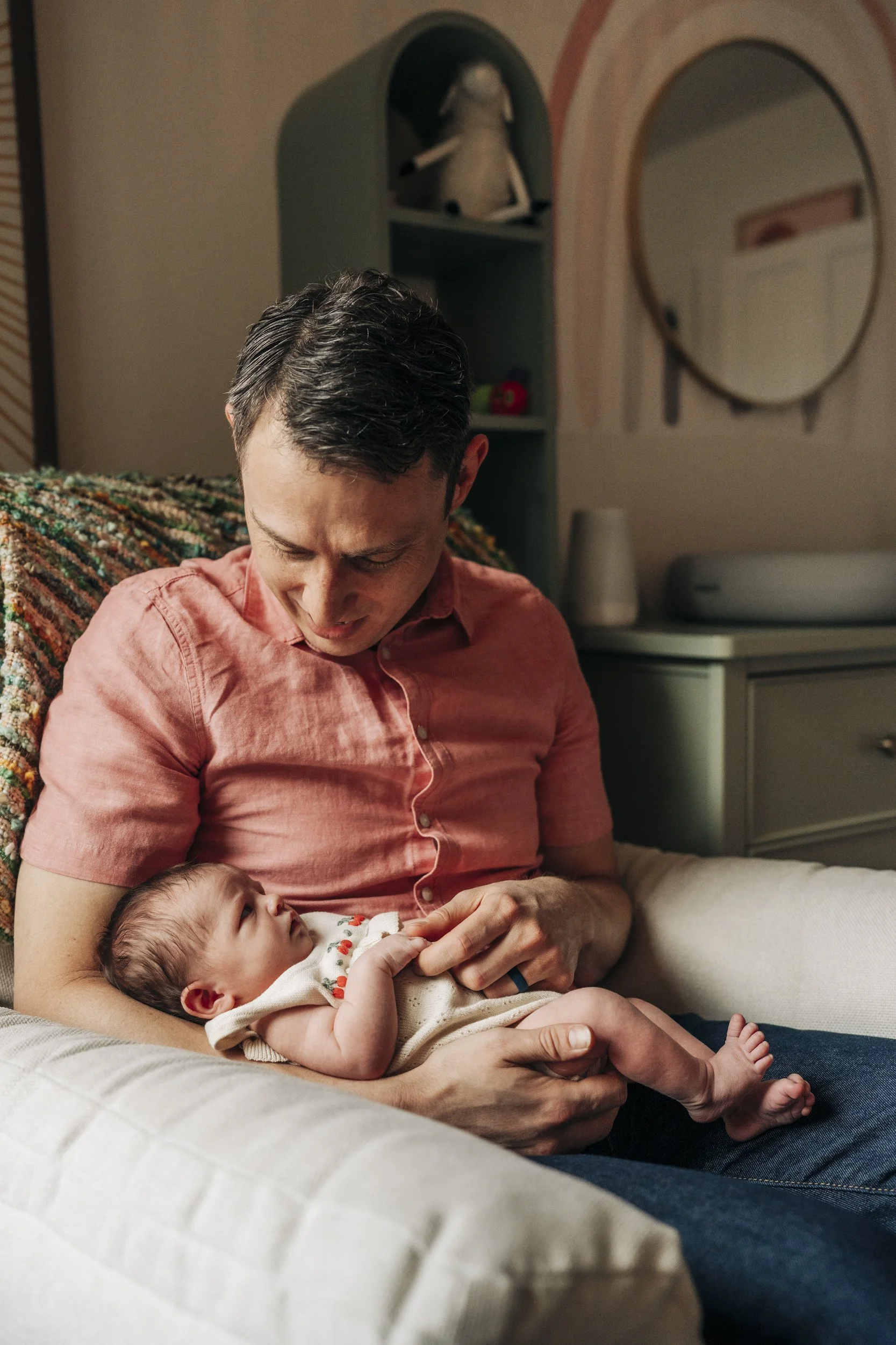 A man holding a newborn baby on a couch in a cozy, warmly lit room.