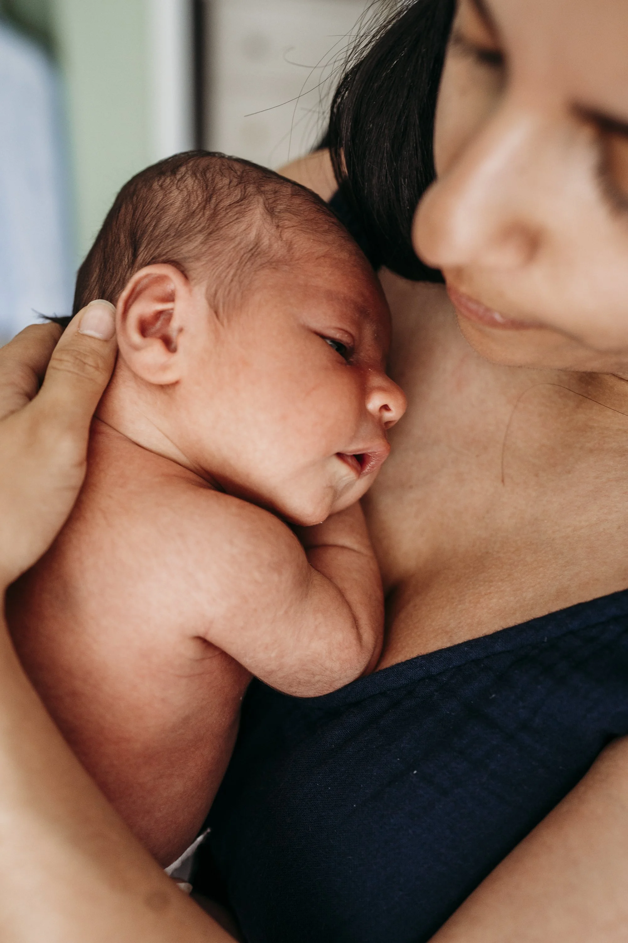 Close-up of a woman holding a newborn baby close to her chest, with their faces touching softly, in an intimate and gentle moment.