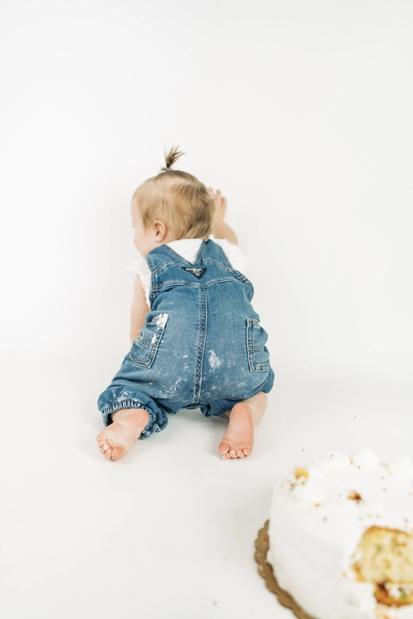Child crawling away on a white floor near a partially visible cake.