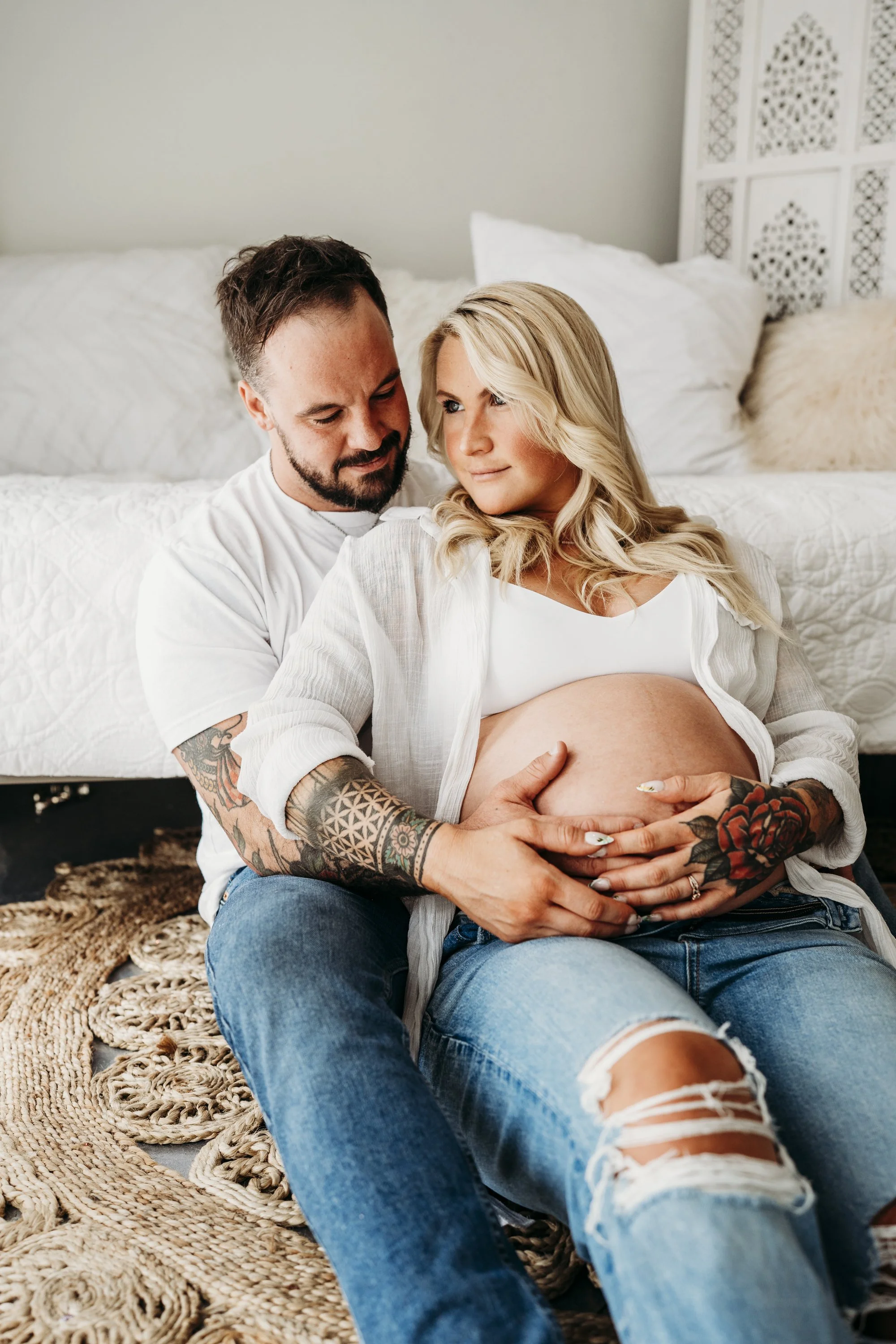 A pregnant woman and her partner sitting on the floor, holding her belly, in a cozy bedroom.