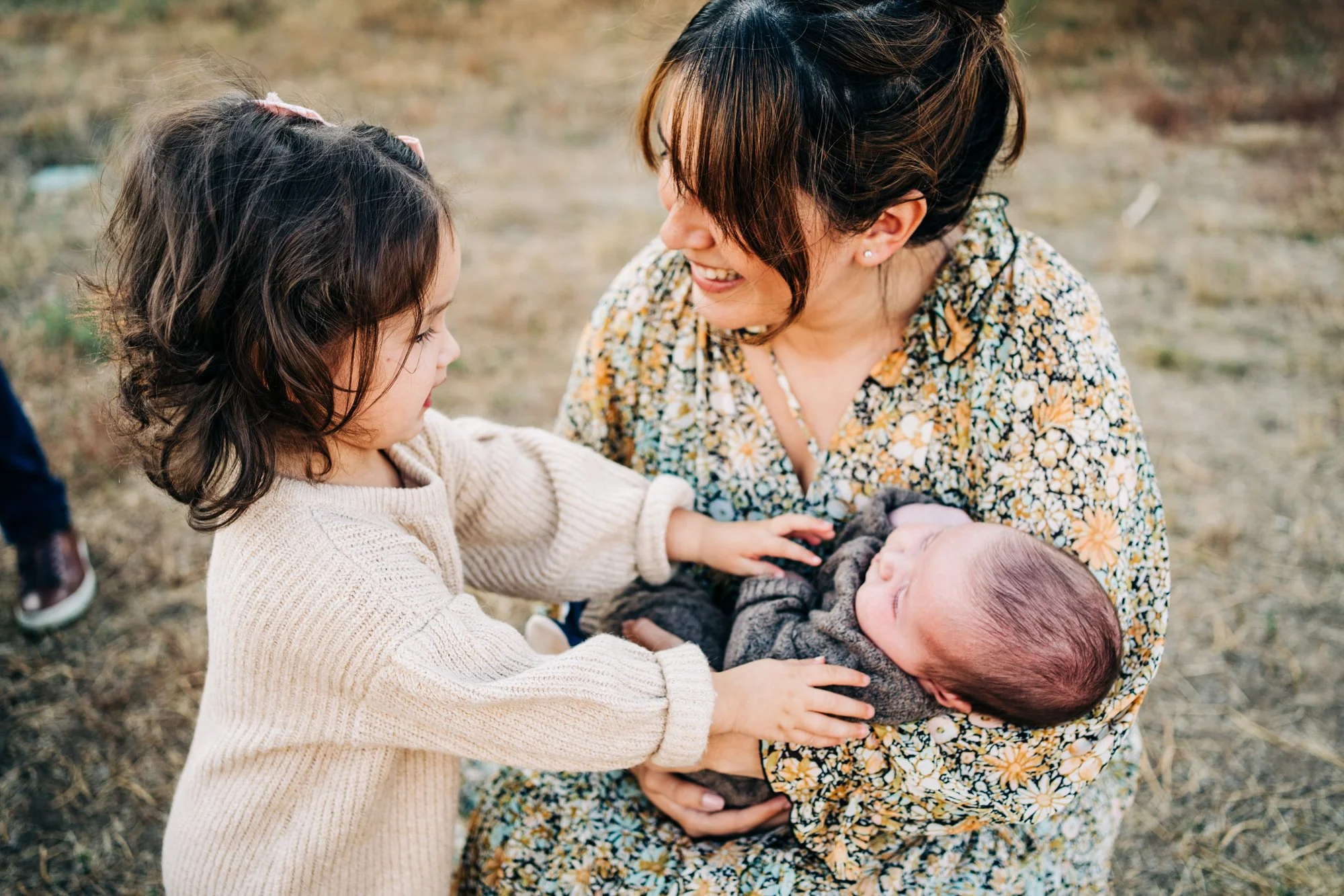 Mother holding newborn with smiling child touching baby outdoors