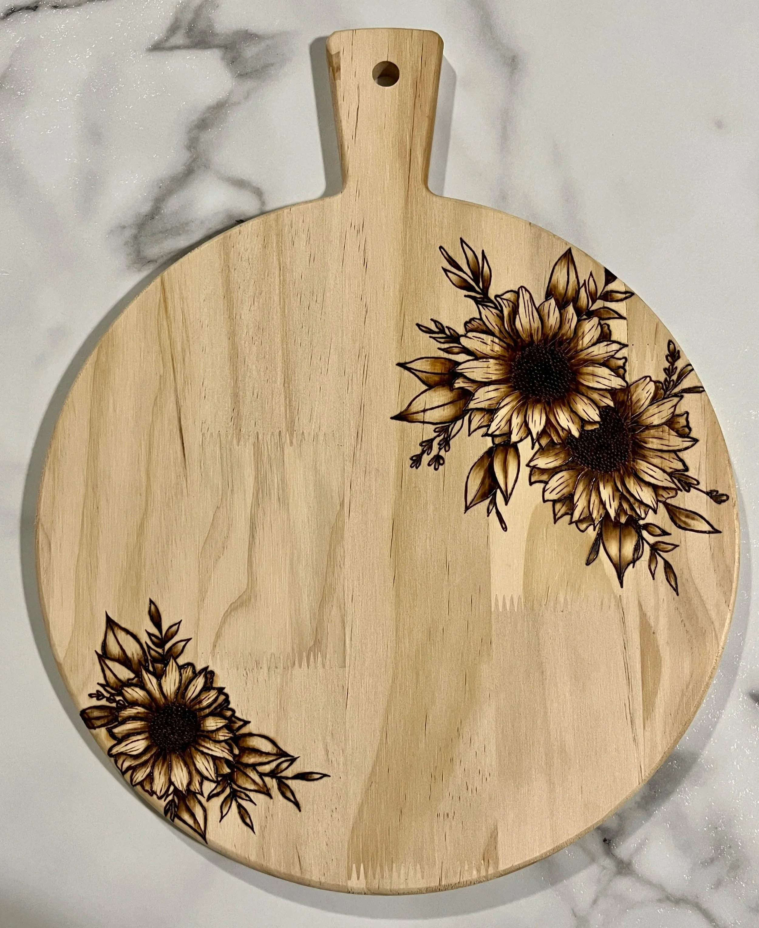 Wood-burned sunflower design featuring three detailed sunflowers with leaves arranged across a round wooden serving board.