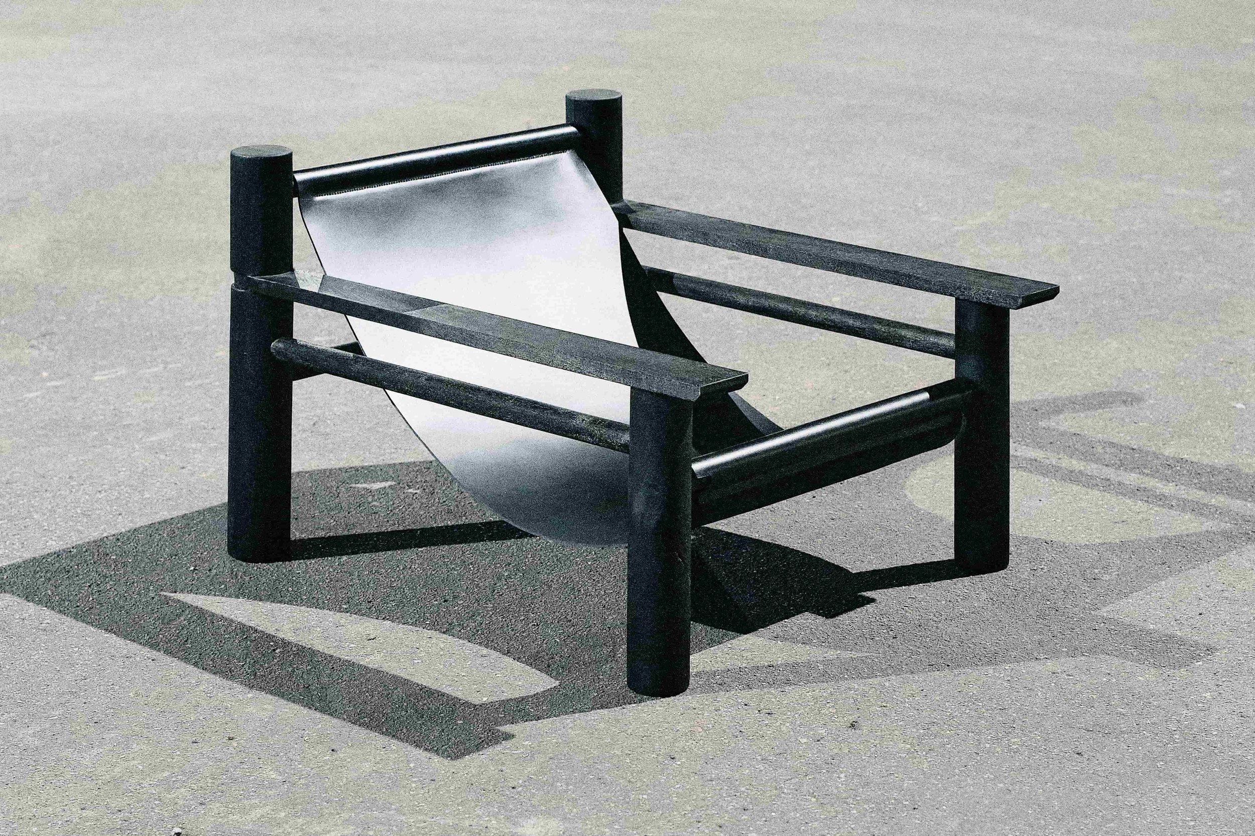 Modern black metal chair with a minimalist design on a concrete surface.