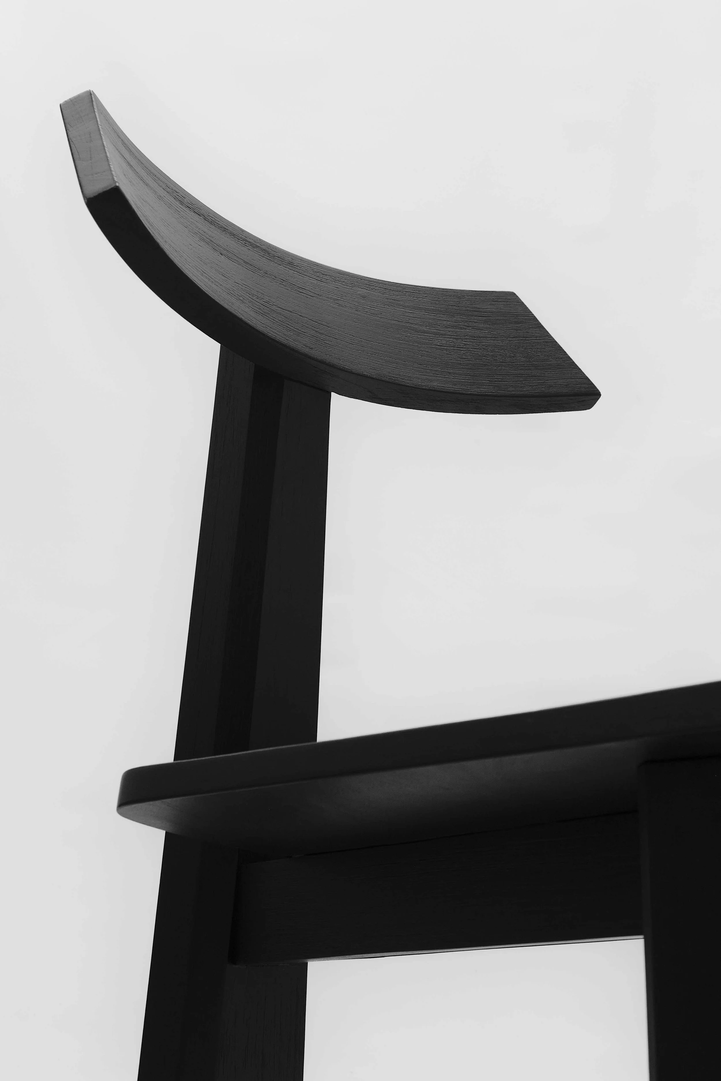 Close-up of a black wooden chair viewed from below, showing the curved top of the backrest against a plain white background.
