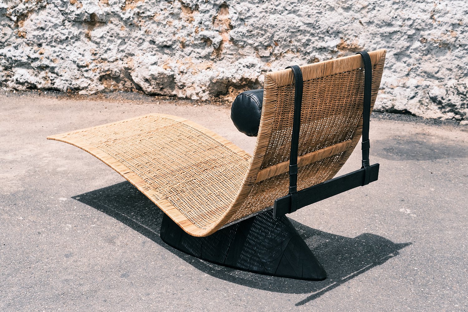 Outdoor wicker chaise lounge with a modern design on a concrete surface, against a textured stone wall background.