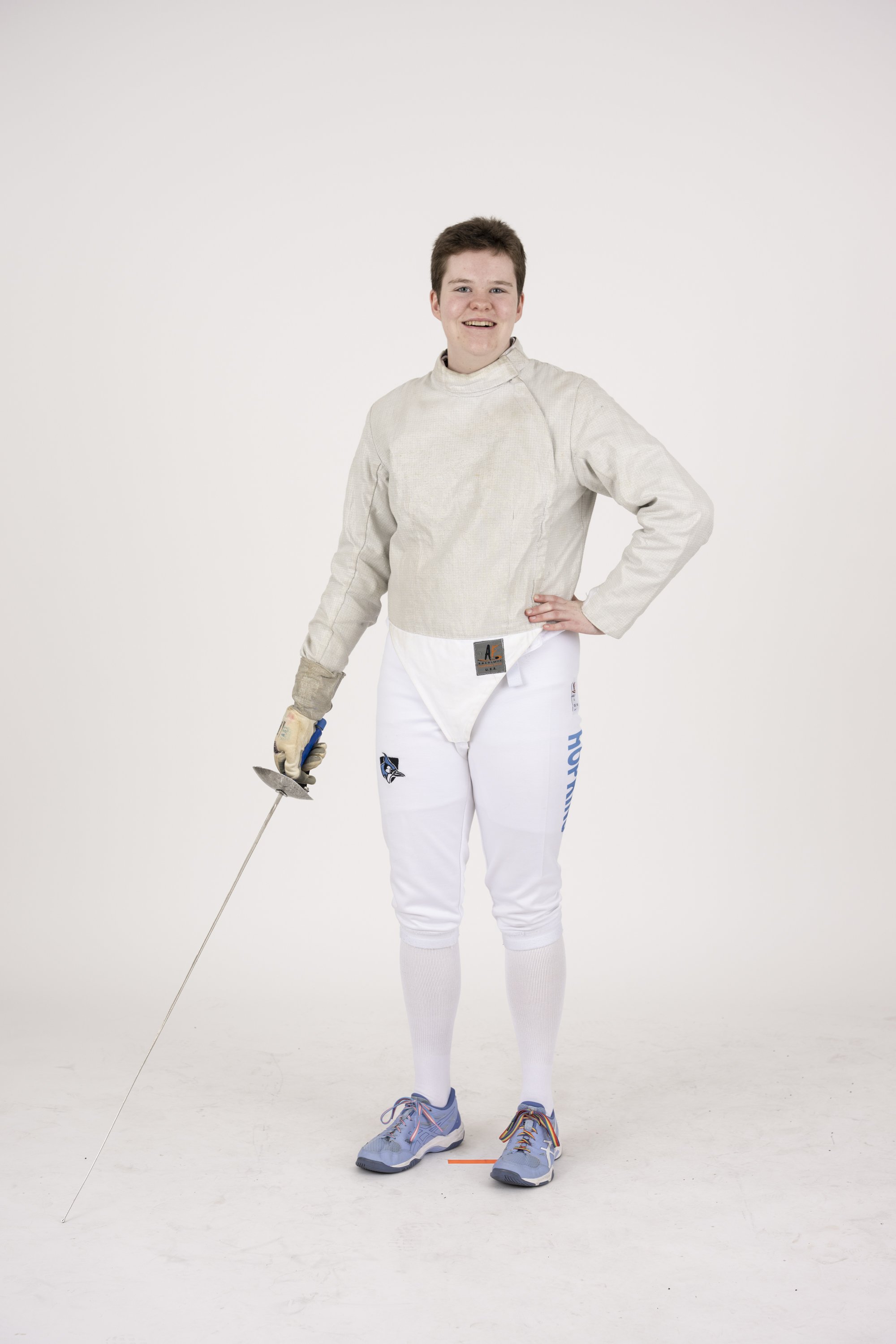 Young male fencer wearing fencing gear, holding a foil, standing on a white background.