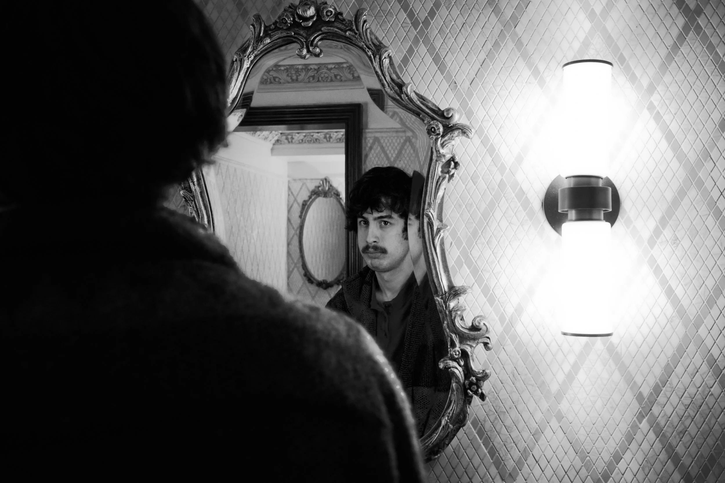 A man in a gym is balancing on one leg on a small platform, with one hand on a rope and the other near his face, performing a fitness exercise.