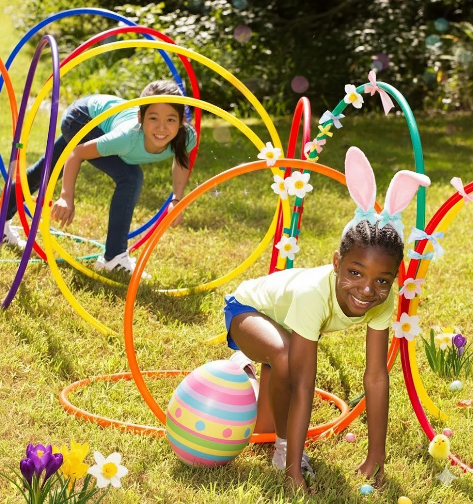 Children playing in an Easter-themed outdoor obstacle course made with colourful hula hoops, wearing bunny ears and face paint during a kids Easter party activity in London.