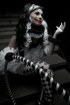 A Halloween hula hoop performer in a black-and-white harlequin-style costume, posing with a striped hoop during a themed event.