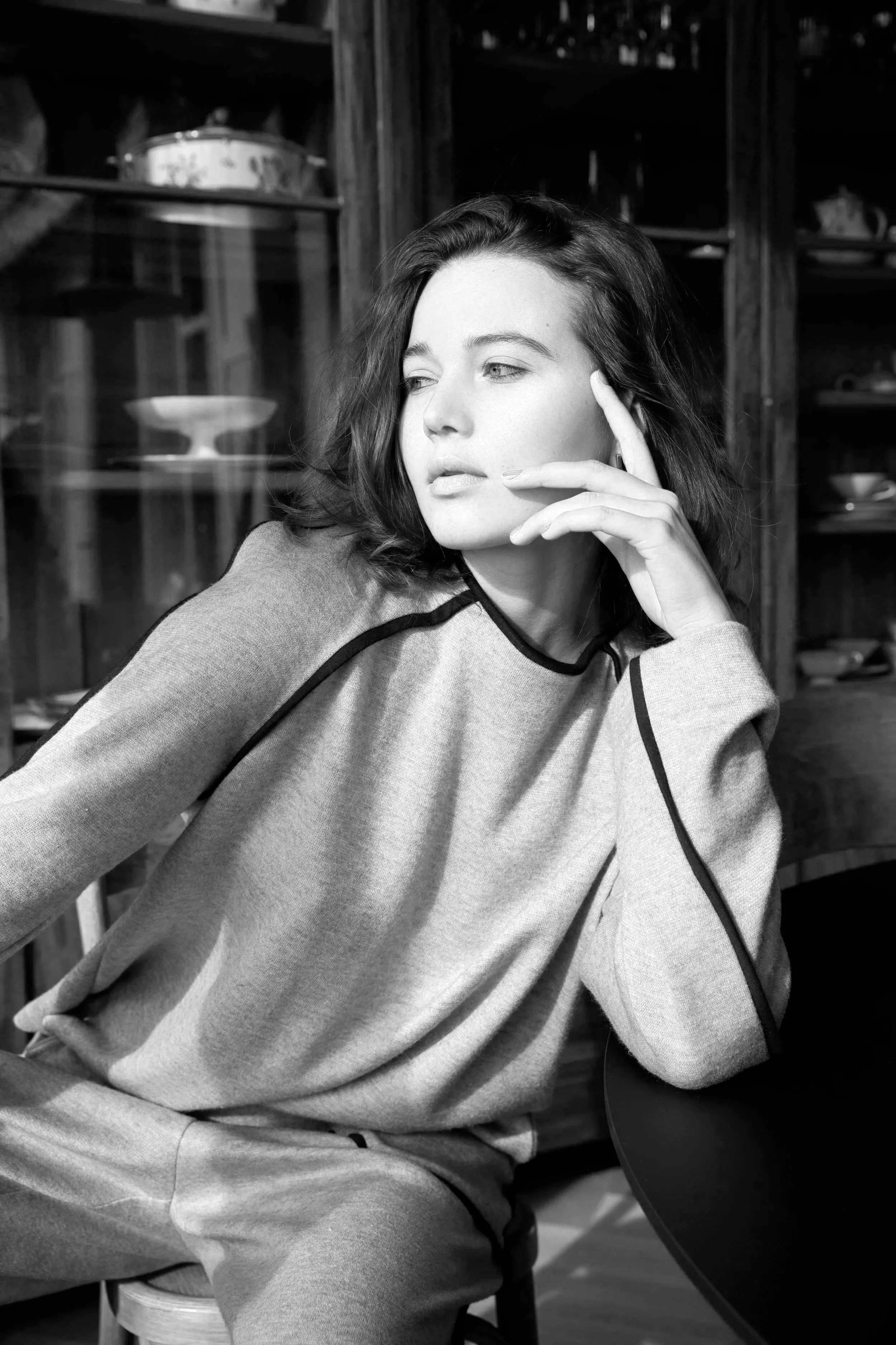 Portrait d'une femme aux cheveux courts, portant un sweat à manches longues, assise à une table dans un décor en bois, regardant vers la gauche.