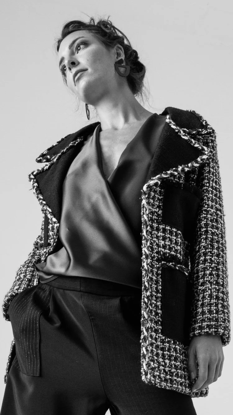 Une femme modèle pose en portant un manteau tweed avec détails en lamé et une blouse en satin, dans un style sophistiqué en noir et blanc.
