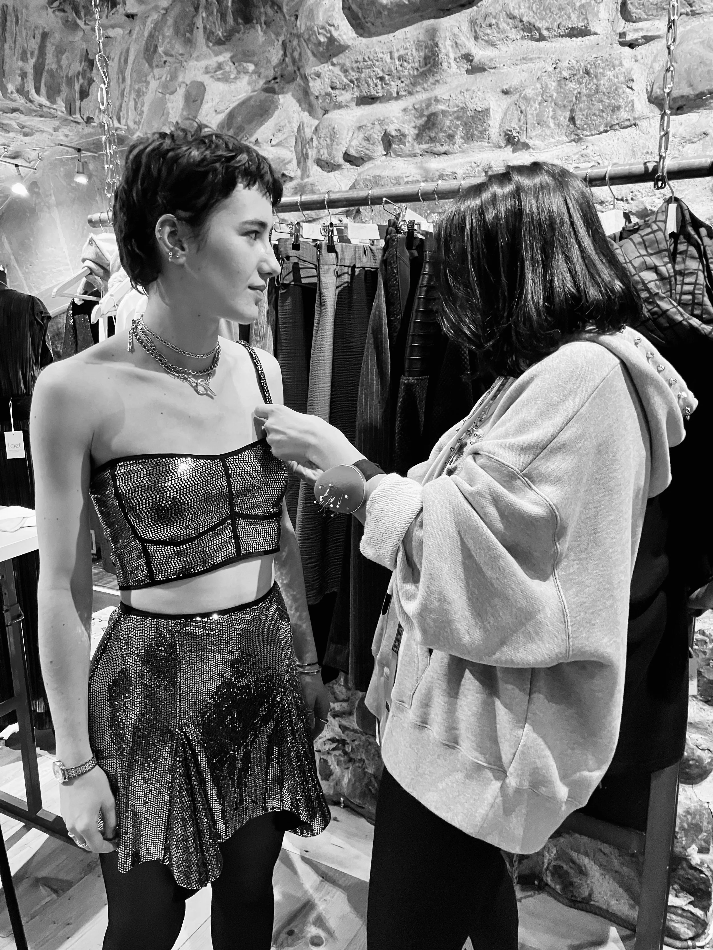 Deux femmes collaborent en train d'essayer ou de montrer des vêtements dans une boutique ou un magasin de vêtements, avec des rayons de vêtements en arrière-plan.