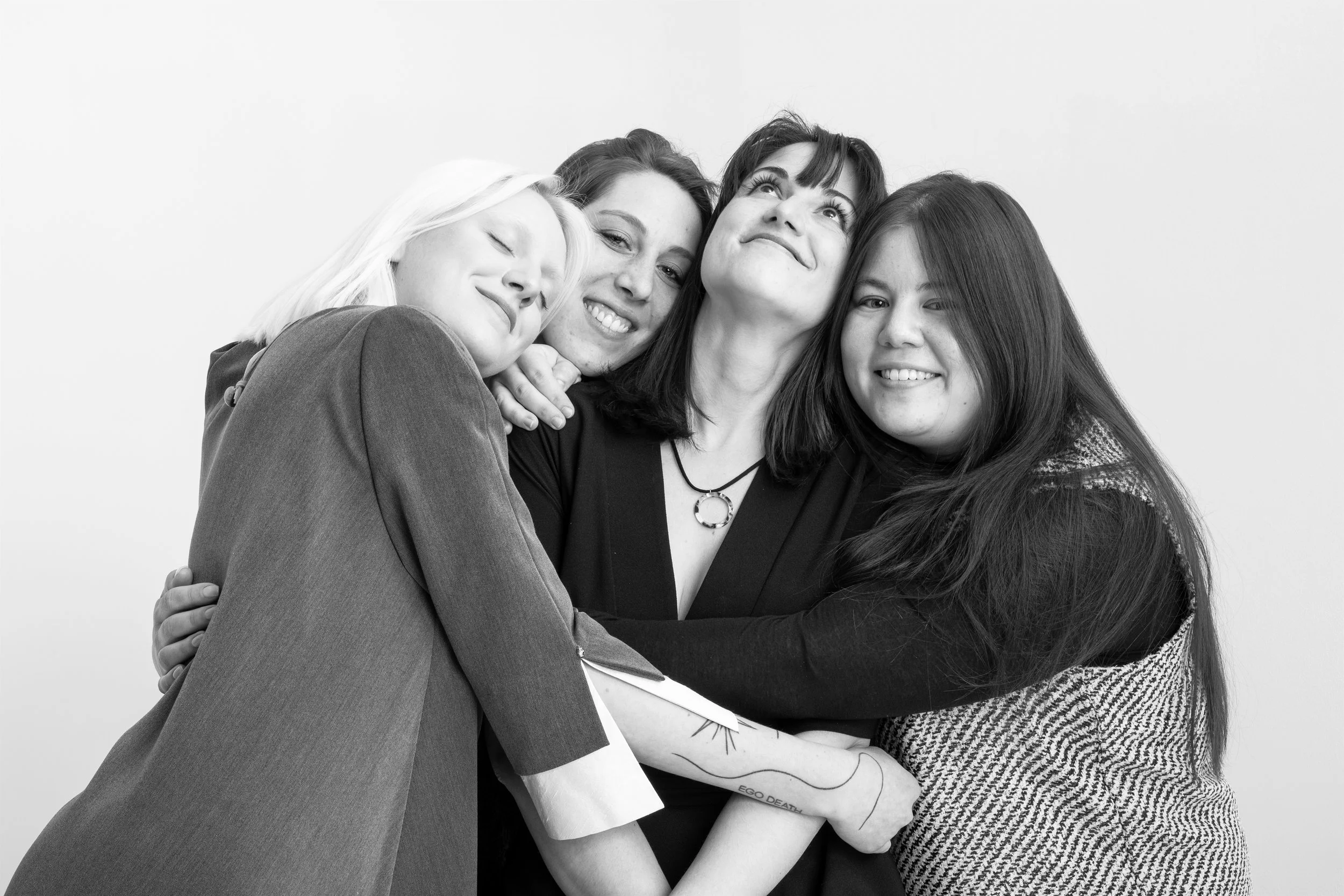 Groupe de quatre jeunes femmes souriantes et visibles en gros plan, en train d'embrasser une poignée de mains ou de se faire un câlin amical, contre un fond blanc