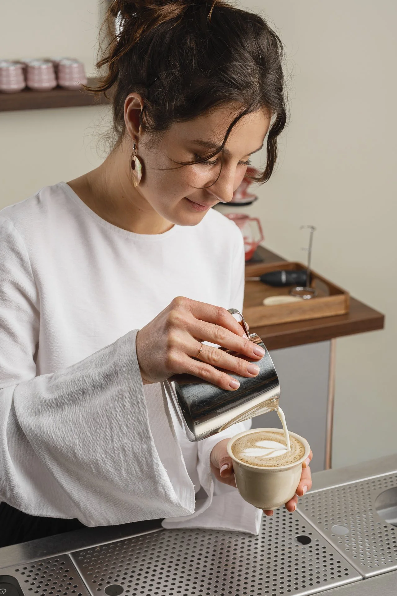 Une femme verse du lait chaud dans une tasse de café latte ou cappuccino, dans une ambiance de café ou de cuisine.