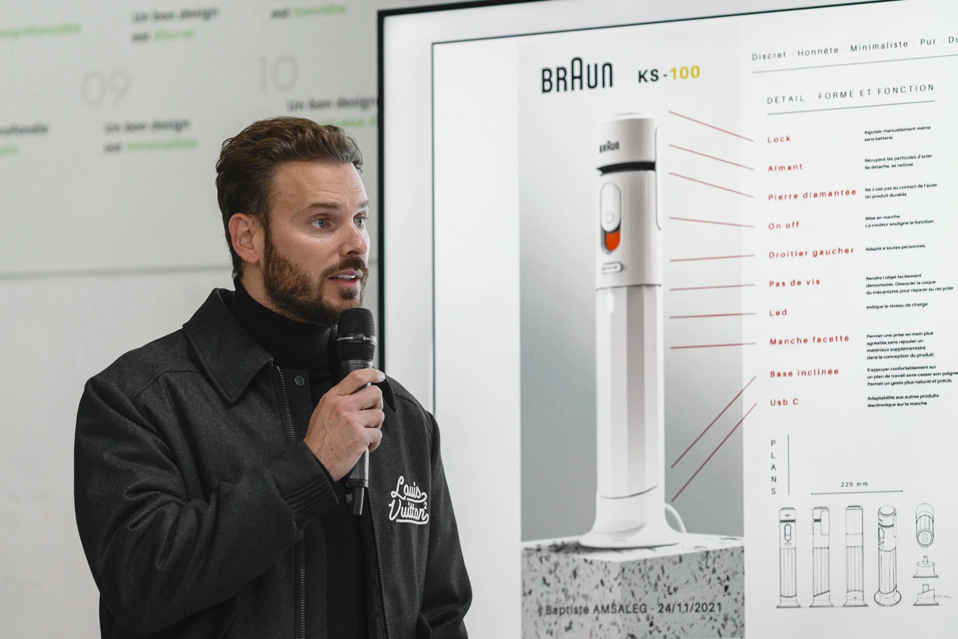 Un homme parlant en tenant un micro lors d'une présentation, avec un panneau d'explication d'un produit électroménager à l'arrière.