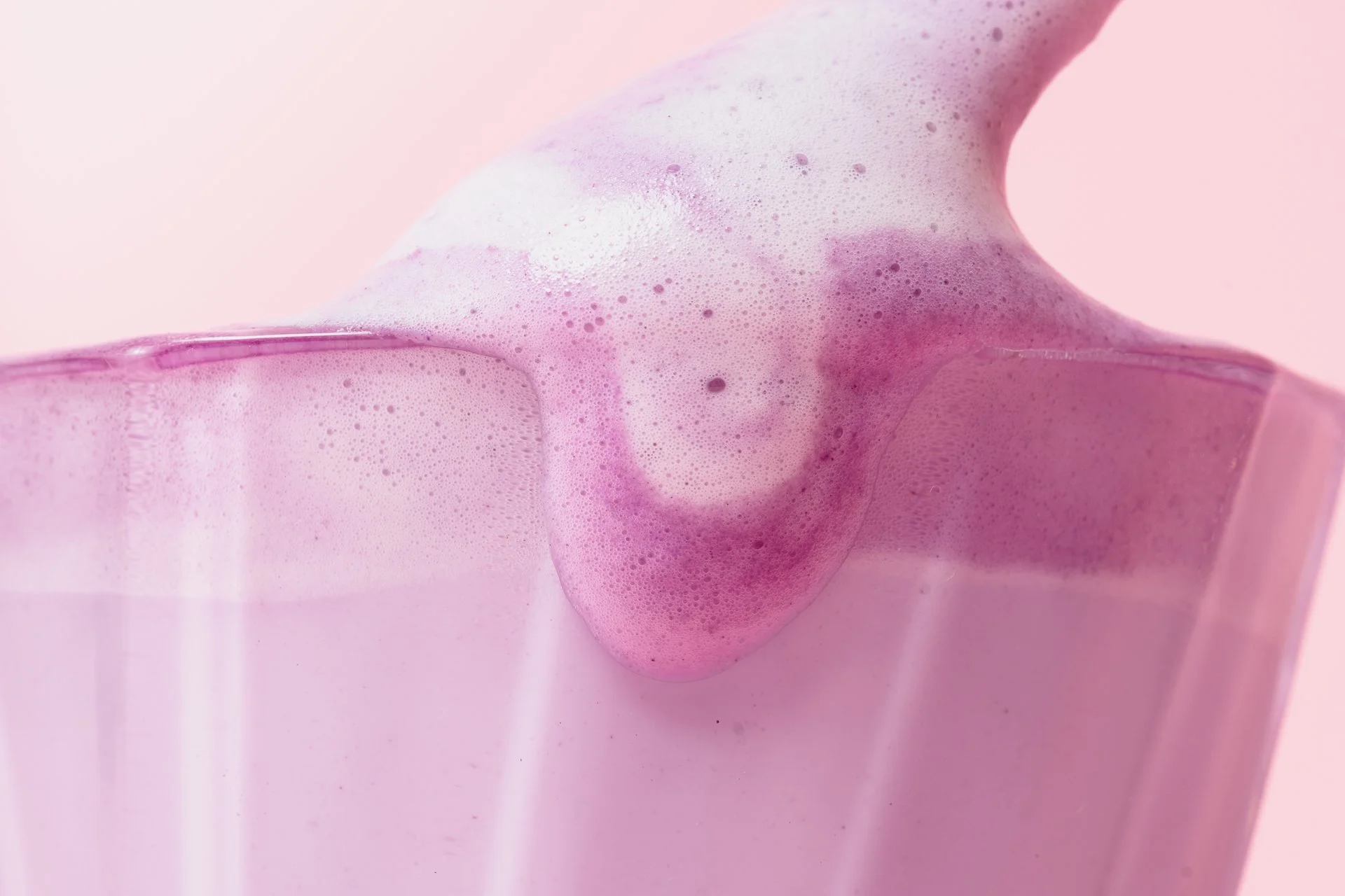 Une boisson rose avec de la mousse dans un verre transparent.