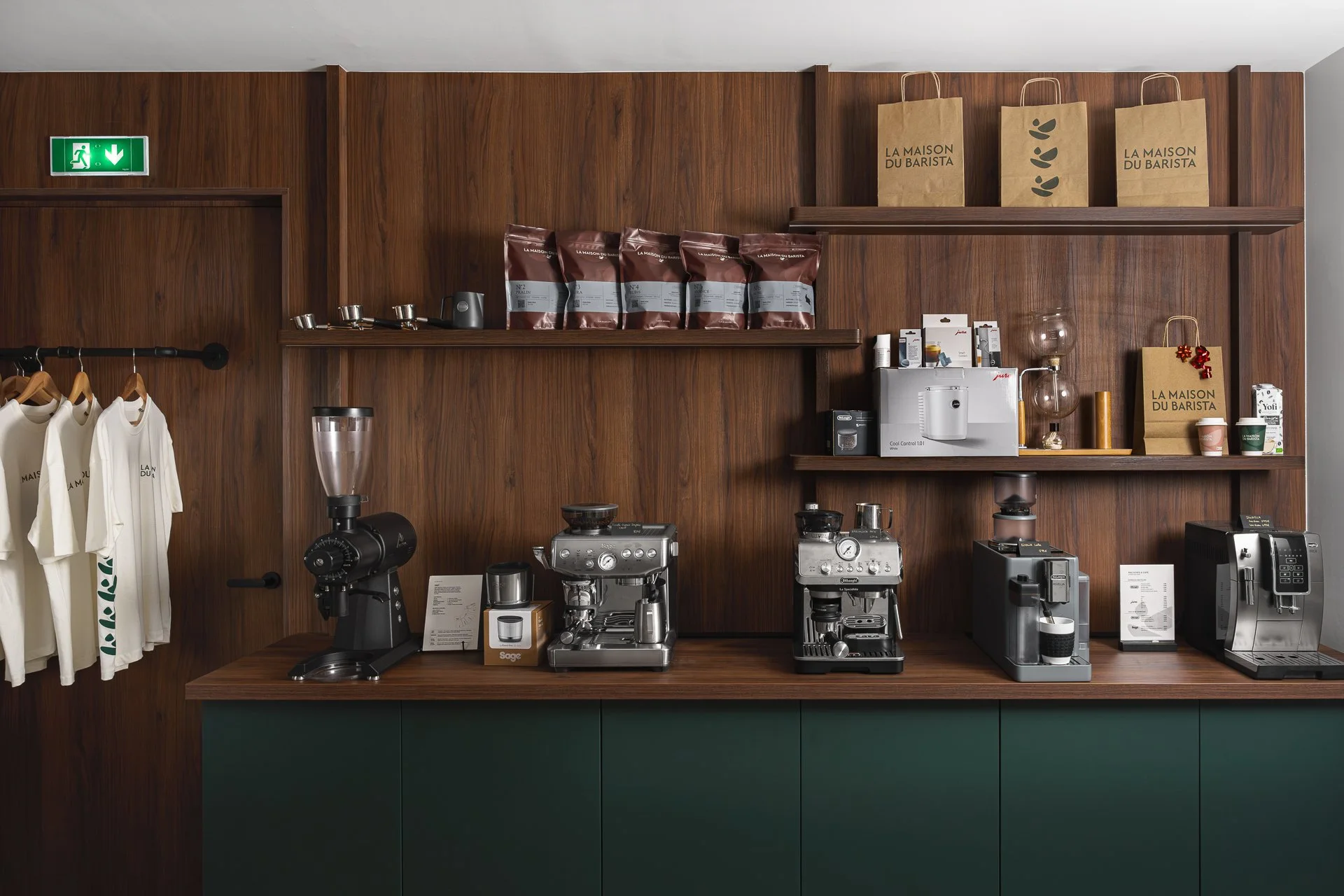 Étagère en bois avec machines à café, sacs de café, t-shirts, téléphones et autres objets liés au café dans un espace de café ou de showroom.