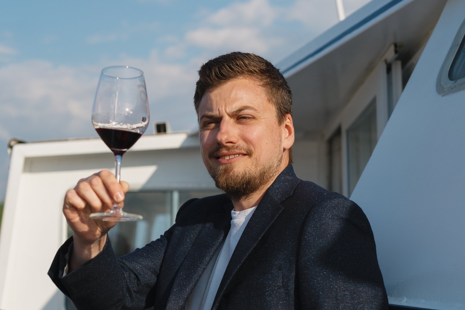 Homme souriant tenant un verre de vin rouge.