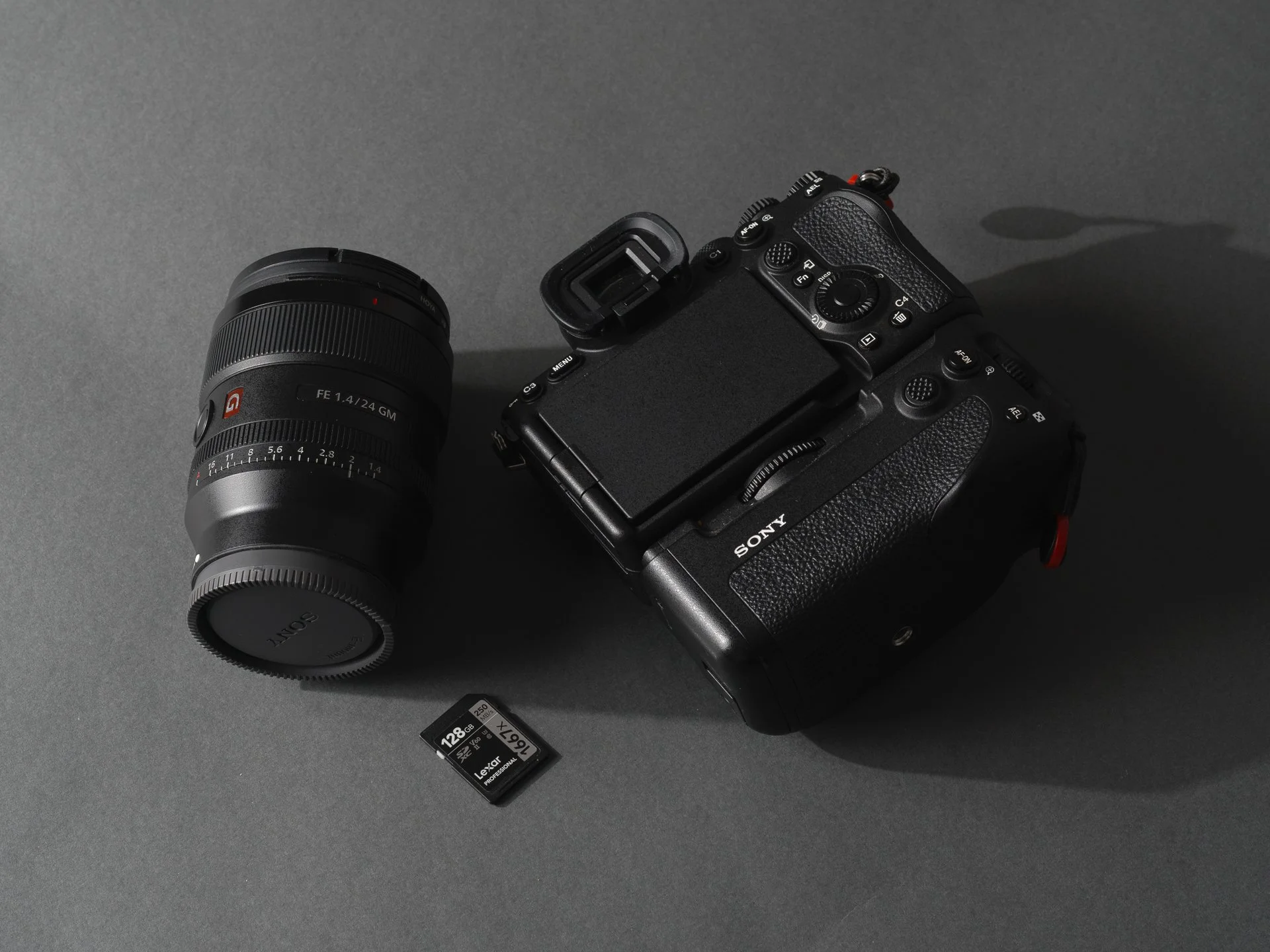 Appareil photo Sony mirrorless noir avec un objectif amovible, une carte mémoire SD Lexar 128 Go placée en dessous, tout sur une surface grise.
