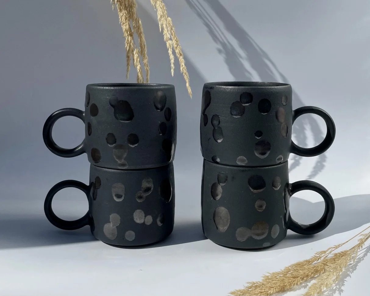 Two stacks of two Dark Moon mugs with satin black glaze and gloss black spots with circular handles on a white backdrop.