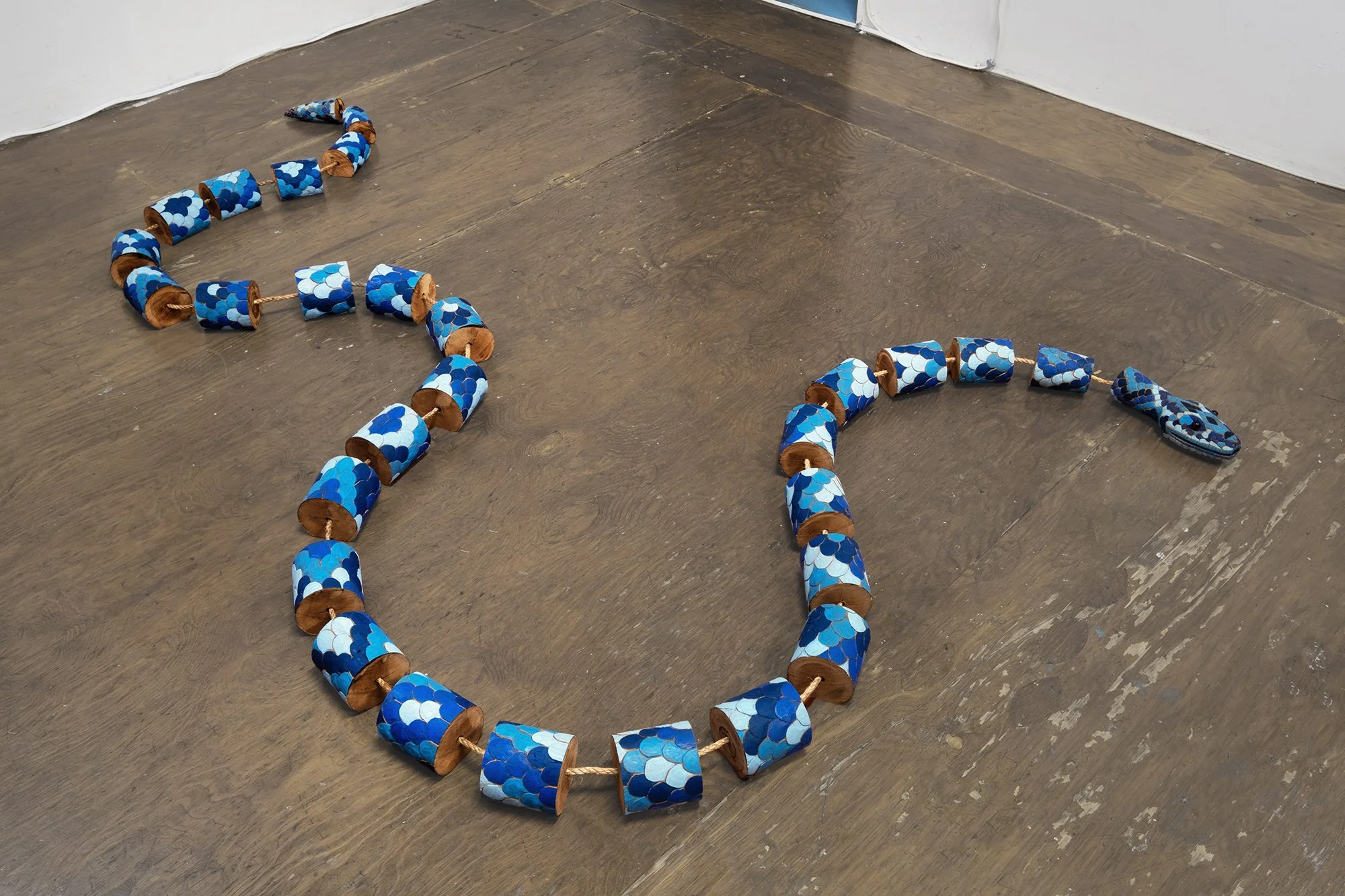 A blue snake sculpture by Matteo Callegari on a brown floor