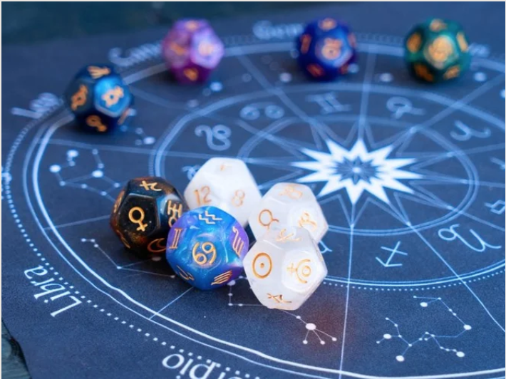 A collection of colorful polyhedral dice placed on a cosmic-themed astrology chart with zodiac signs and constellation patterns.