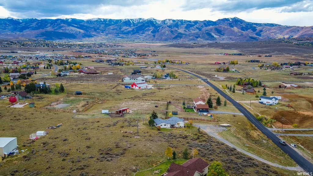 Aerial view of a rural landscape with scattered houses, roads, and open fields, set against a backdrop of mountains under a cloudy sky.