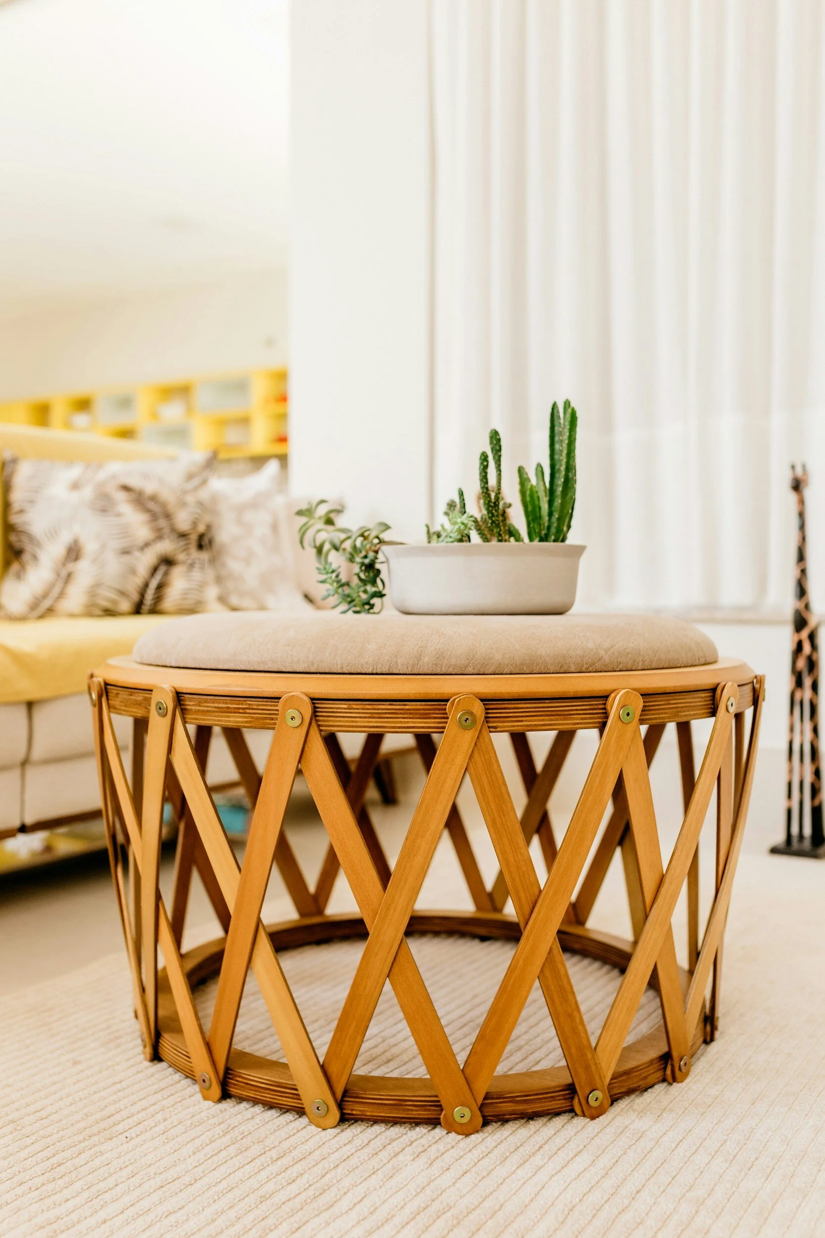 Modern wooden coffee table with lattice design, topped with a beige cushion and a potted cactus, in a bright living room setting.