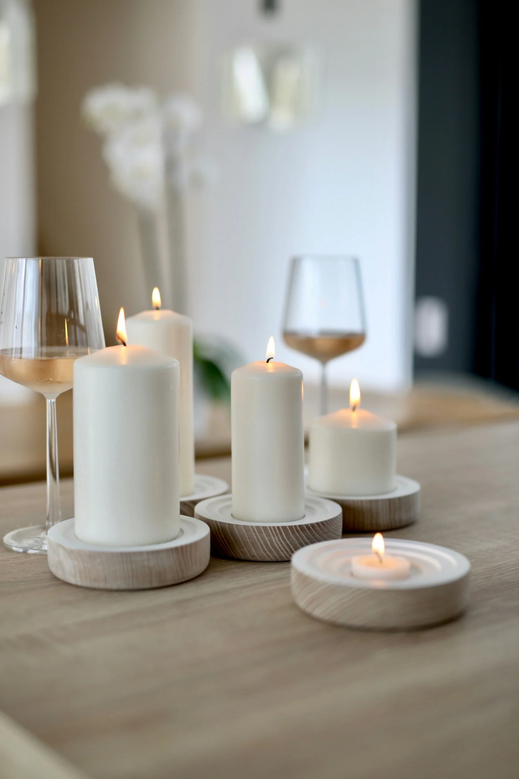 Lit candles on wooden holders and wine glasses on a wooden table.