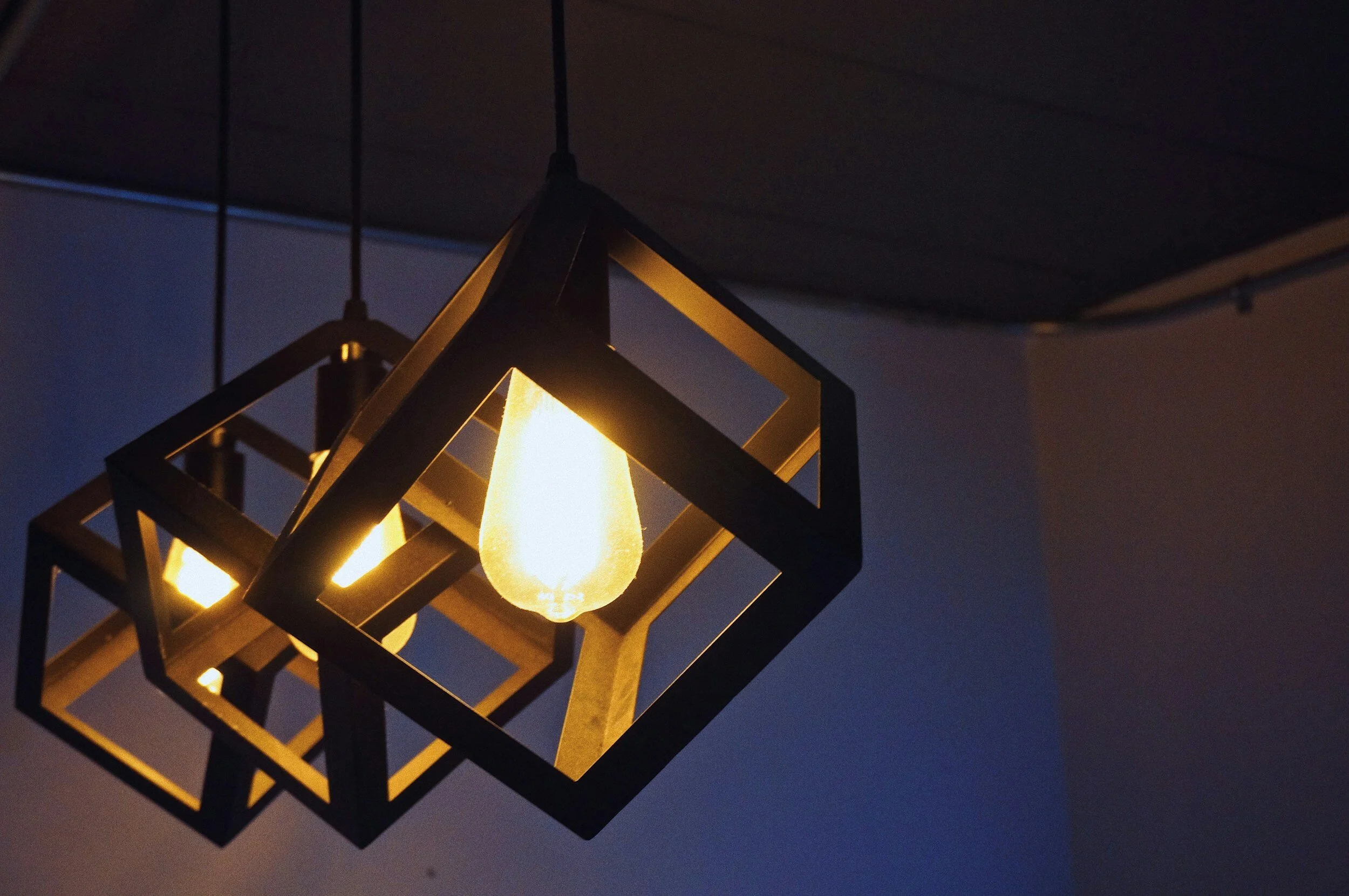 Modern pendant lights with geometric frames and exposed bulbs, dimly lit.