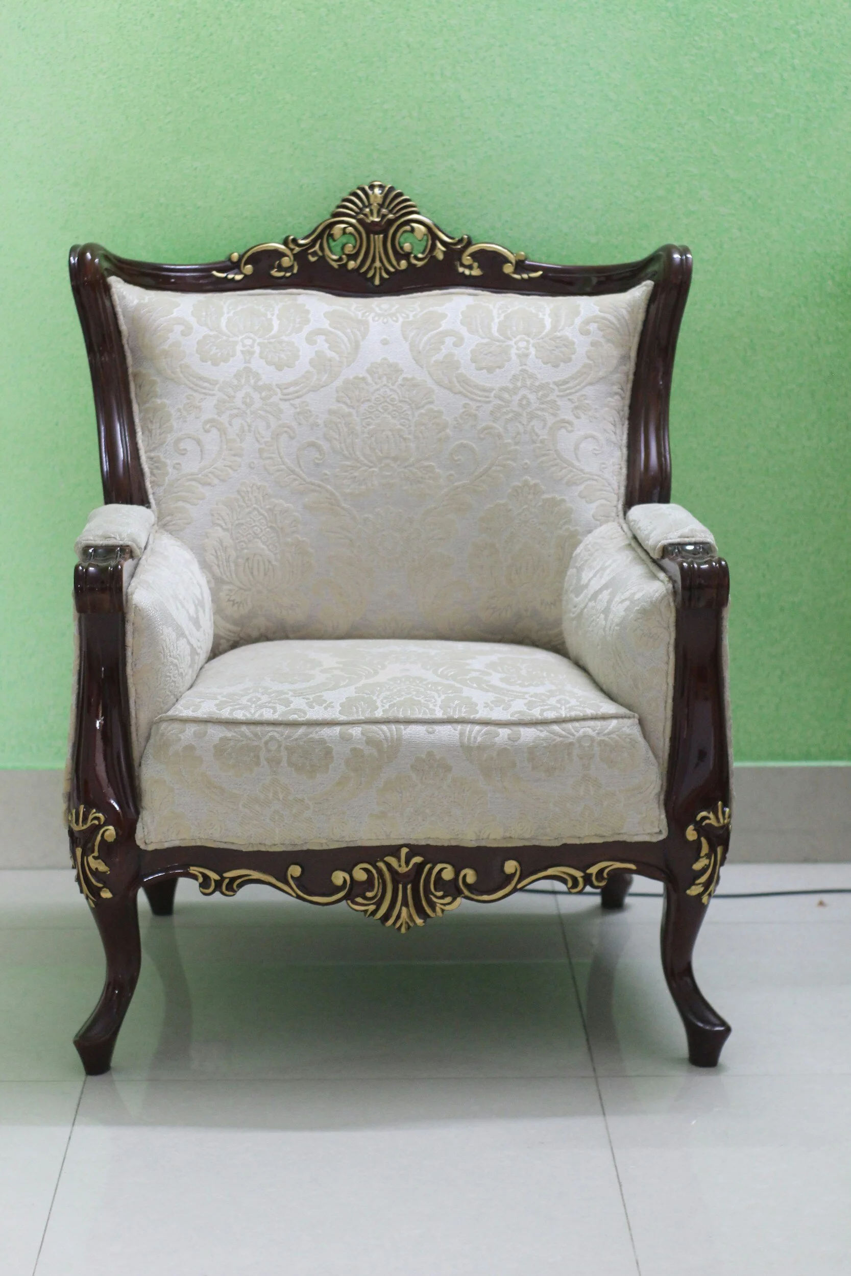 Vintage upholstered armchair with ornate wood carving against a green wall
