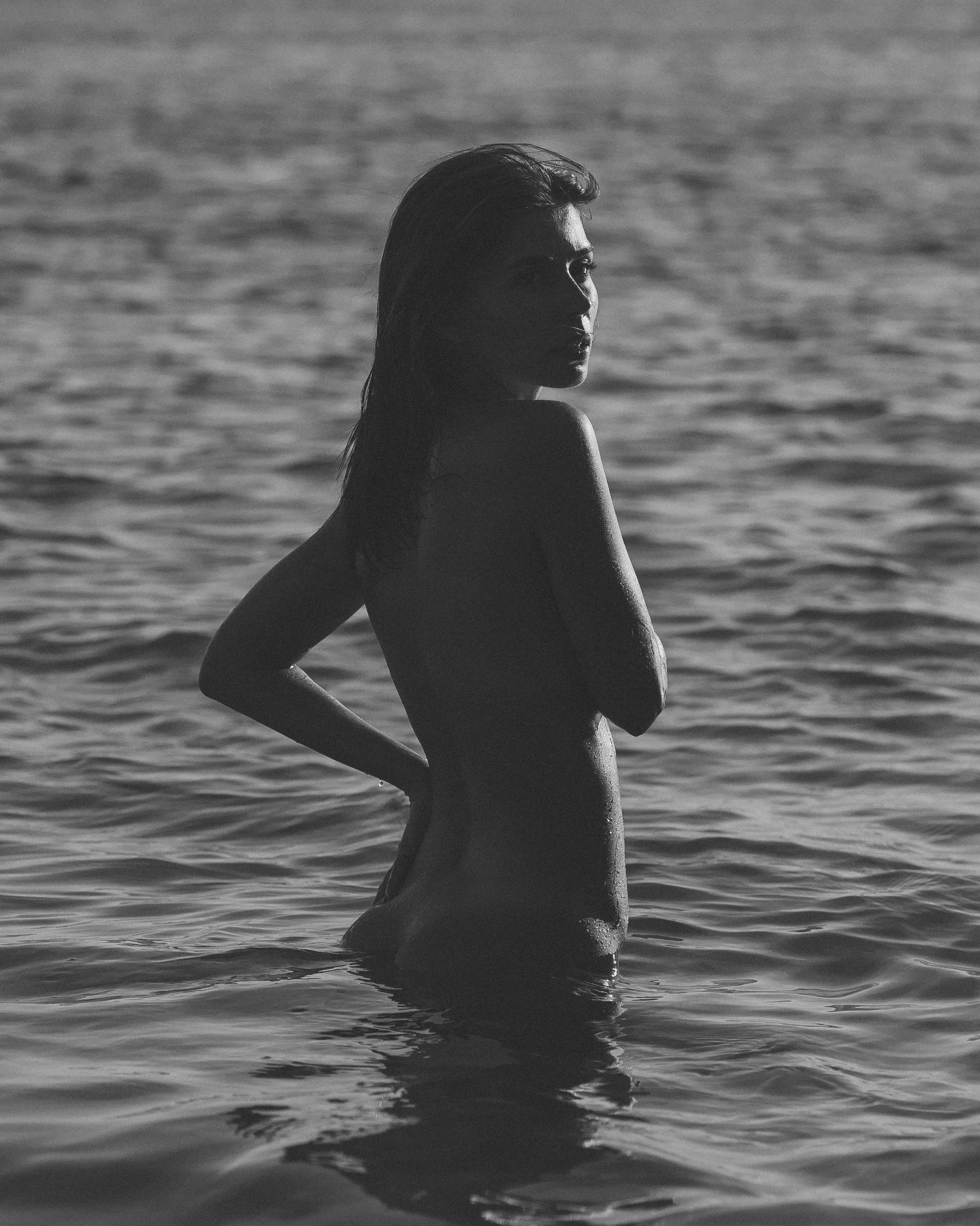 A woman with wet hair standing in water, facing sideways with her face partially visible, in black and white.
