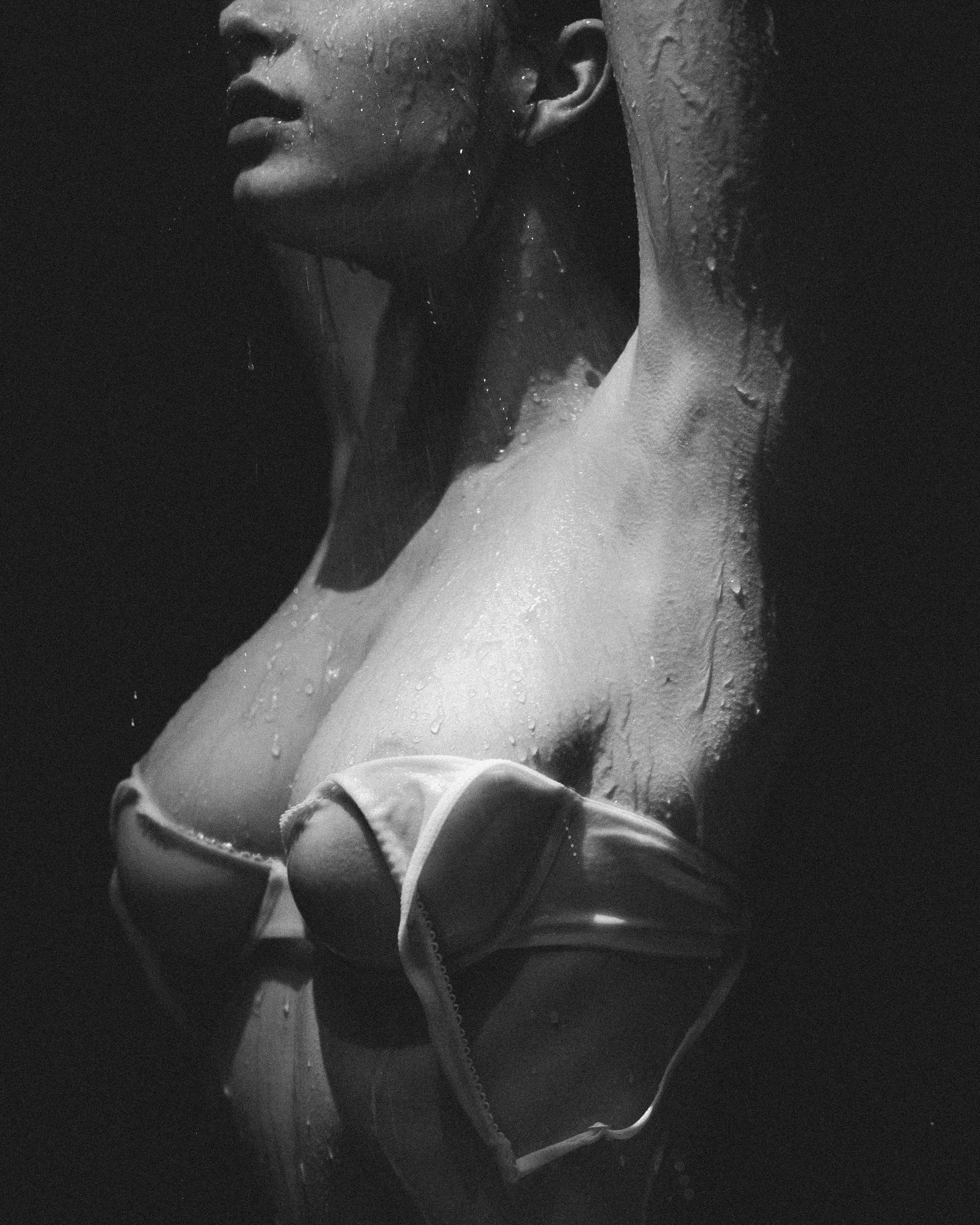 Close-up black and white photo of a person's face and upper body with water droplets on skin, and earphones around neck.