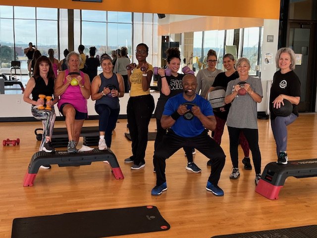 Class photo of the fitness instructor and his class posing for a photo with dumbbells, medicine balls and kettlebells in hand.