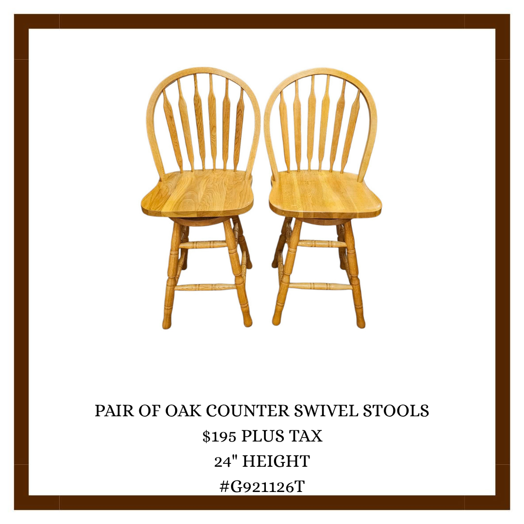 Two wooden oak counter swivel stools with slatted backs and slightly curved seats, placed side by side on a white background.