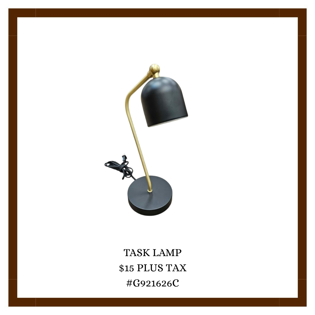 A black and gold task lamp with a black lampshade on a white background, displayed on a promotional sign that reads: 'TASK LAMP, $15 PLUS TAX, #G921626C'.