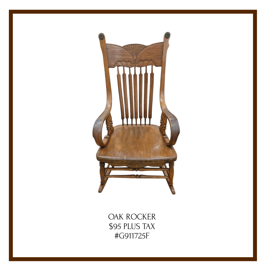 A wooden oak rocking chair with high back and armrests, carved details, and spindle design, against a white background, with a brown border around the image.