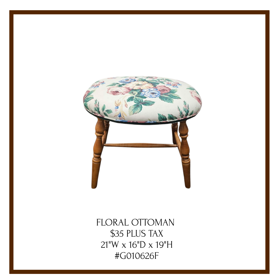 A floral upholstered ottoman with wooden legs. The fabric features a pattern of multicolored flowers. The ottoman is displayed in a catalog with details about pricing and dimensions.