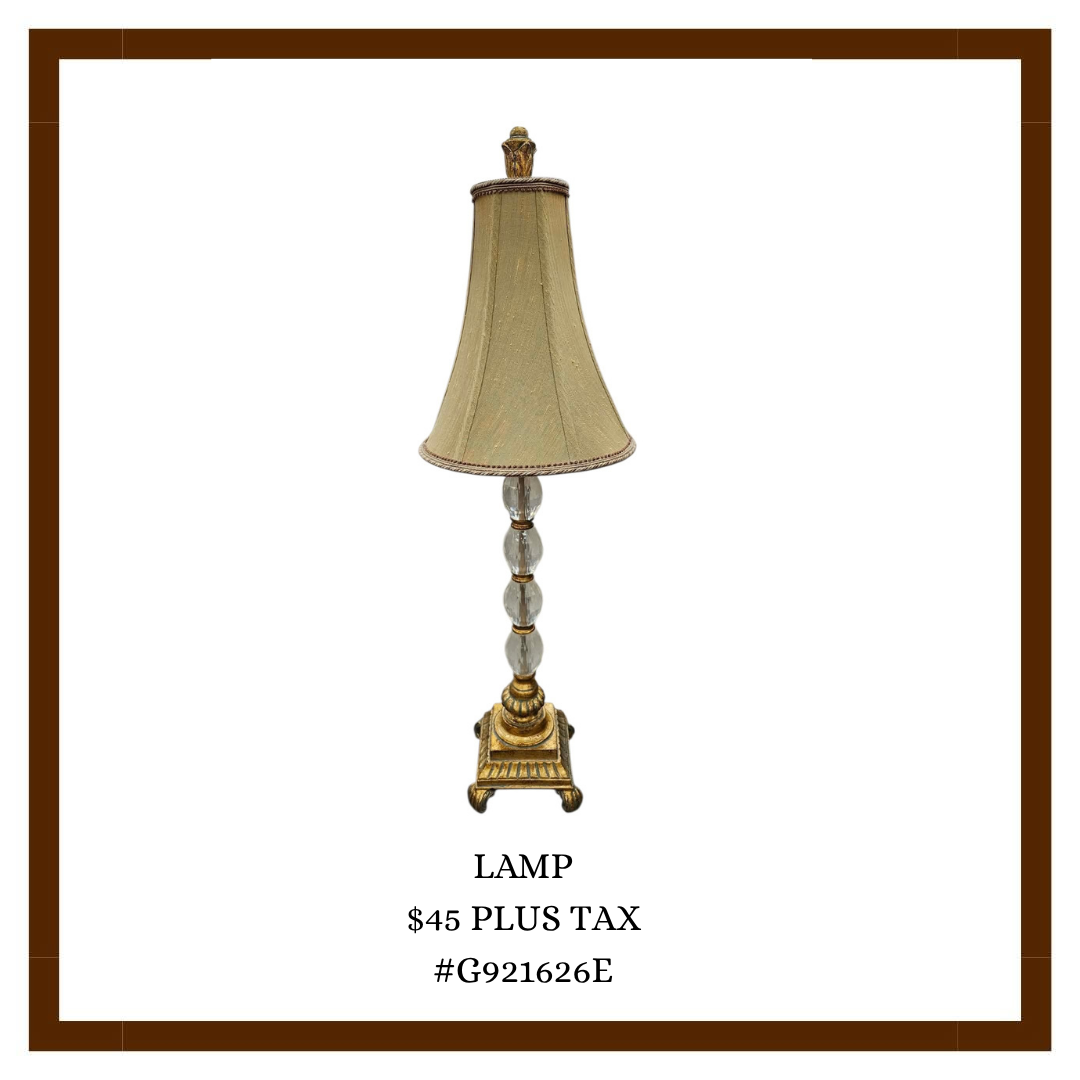 A vintage-style table lamp with a beige lampshade, decorative glass and gold-colored base, and a finial on top, listed for $45 plus tax with a product code #G921626E.